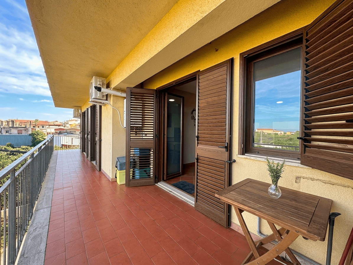 Balcone ampio con vista sulla città, arredato con tavolo in legno e piante, ideale per relax e convivialità.
