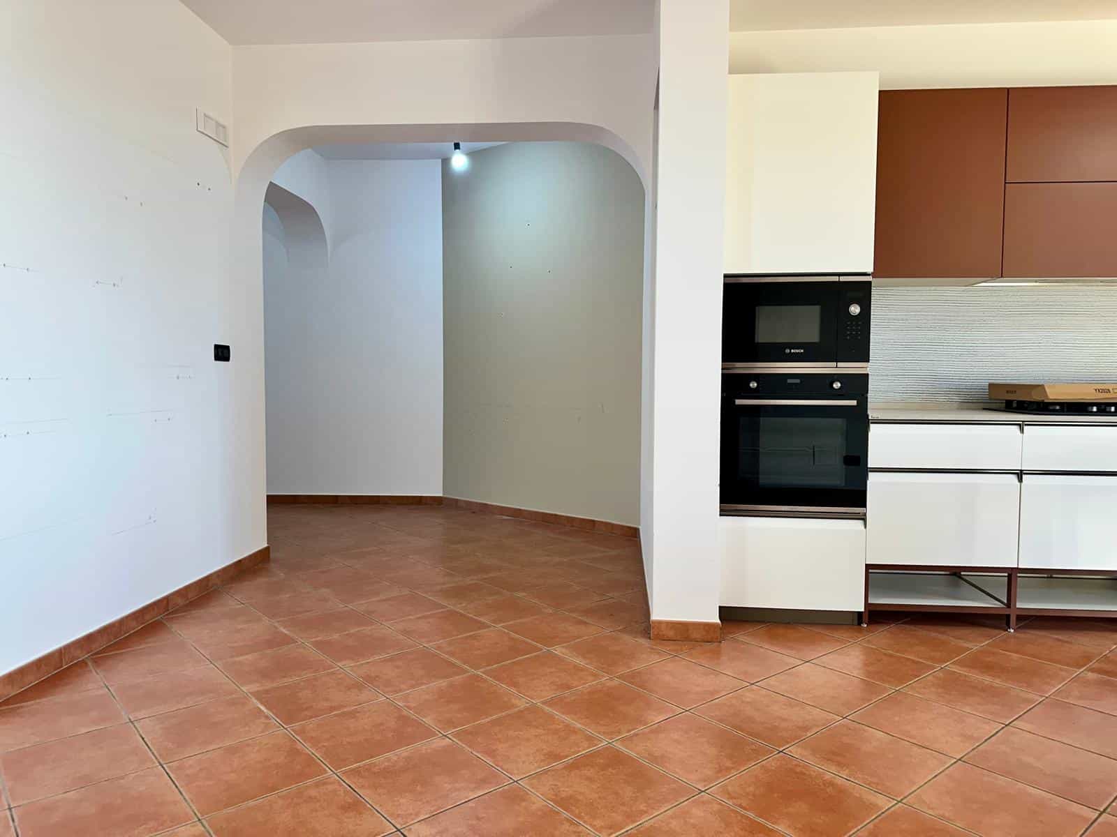 Cucina moderna con mobili bianchi e pareti in tonalità neutre, pavimento in piastrelle terracotta, spazio luminoso e accogliente, ideale per la vita quotidiana e la convivialità.