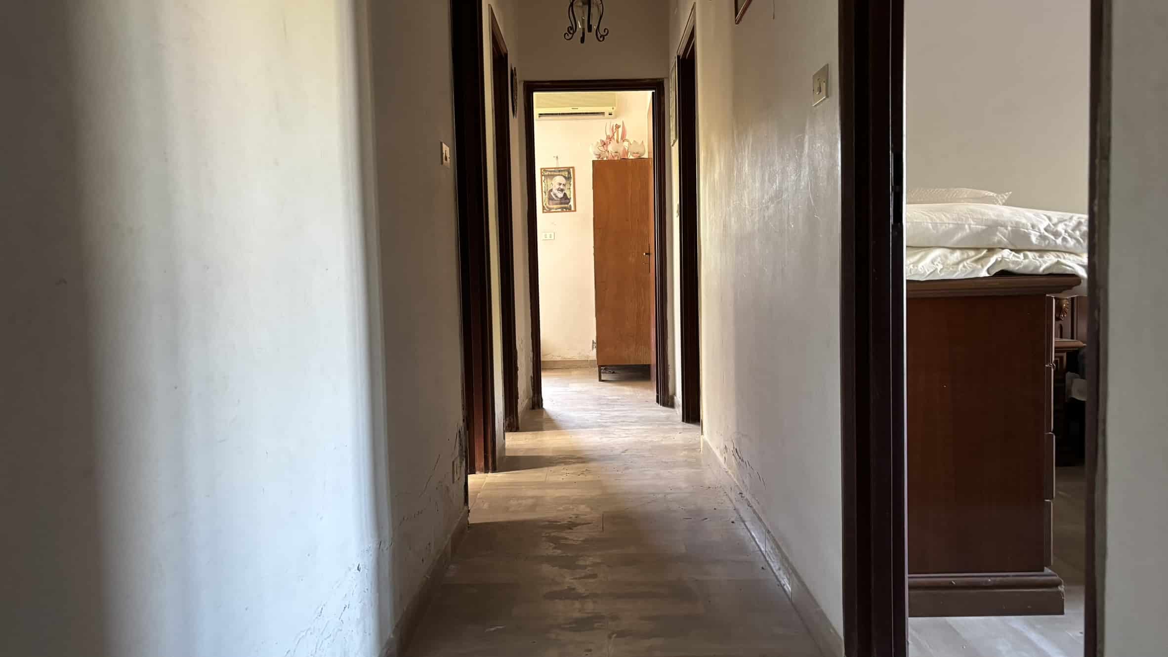 Corridoio interno di casa con pavimento in legno e pareti verniciate in colore chiaro, visibile in una residenza abitativa consolidata e autentica.