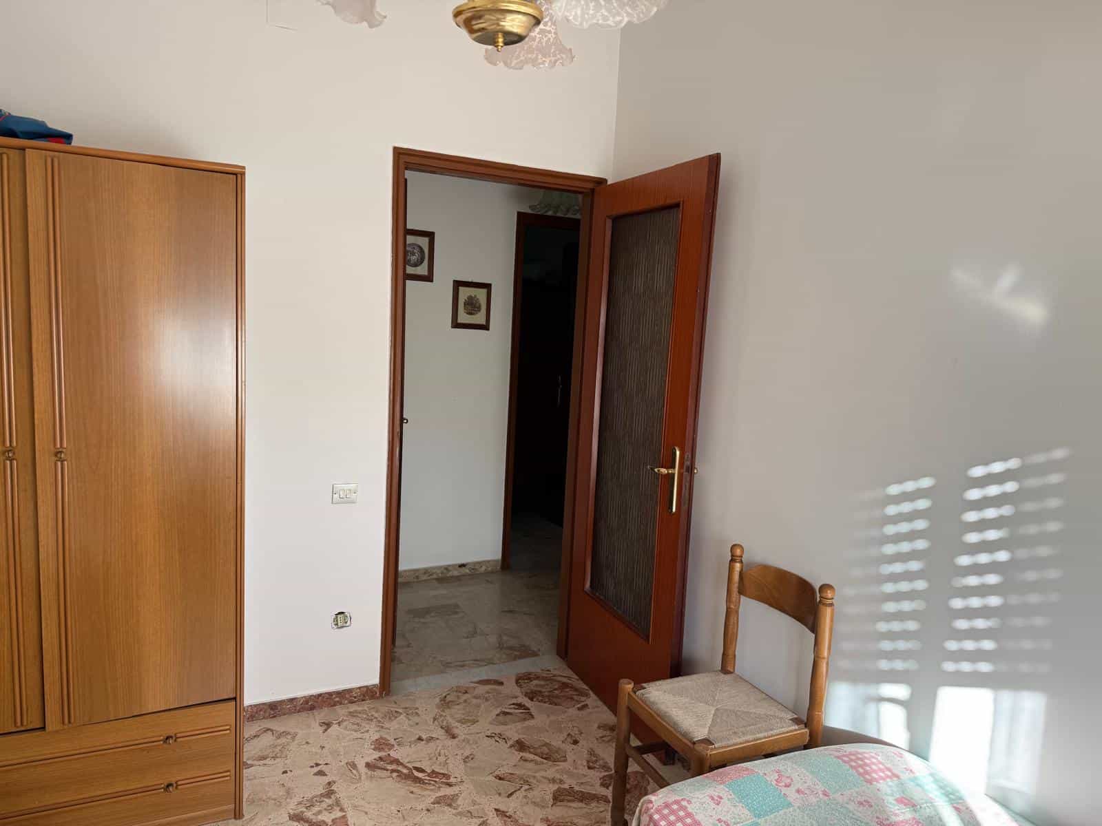 Armadio in legno e porta in stile classico, camera da letto con pareti bianche e pavimento in marmo, spazio accogliente e funzionale, illuminato dalla luce naturale attraverso una finestra con persiane.