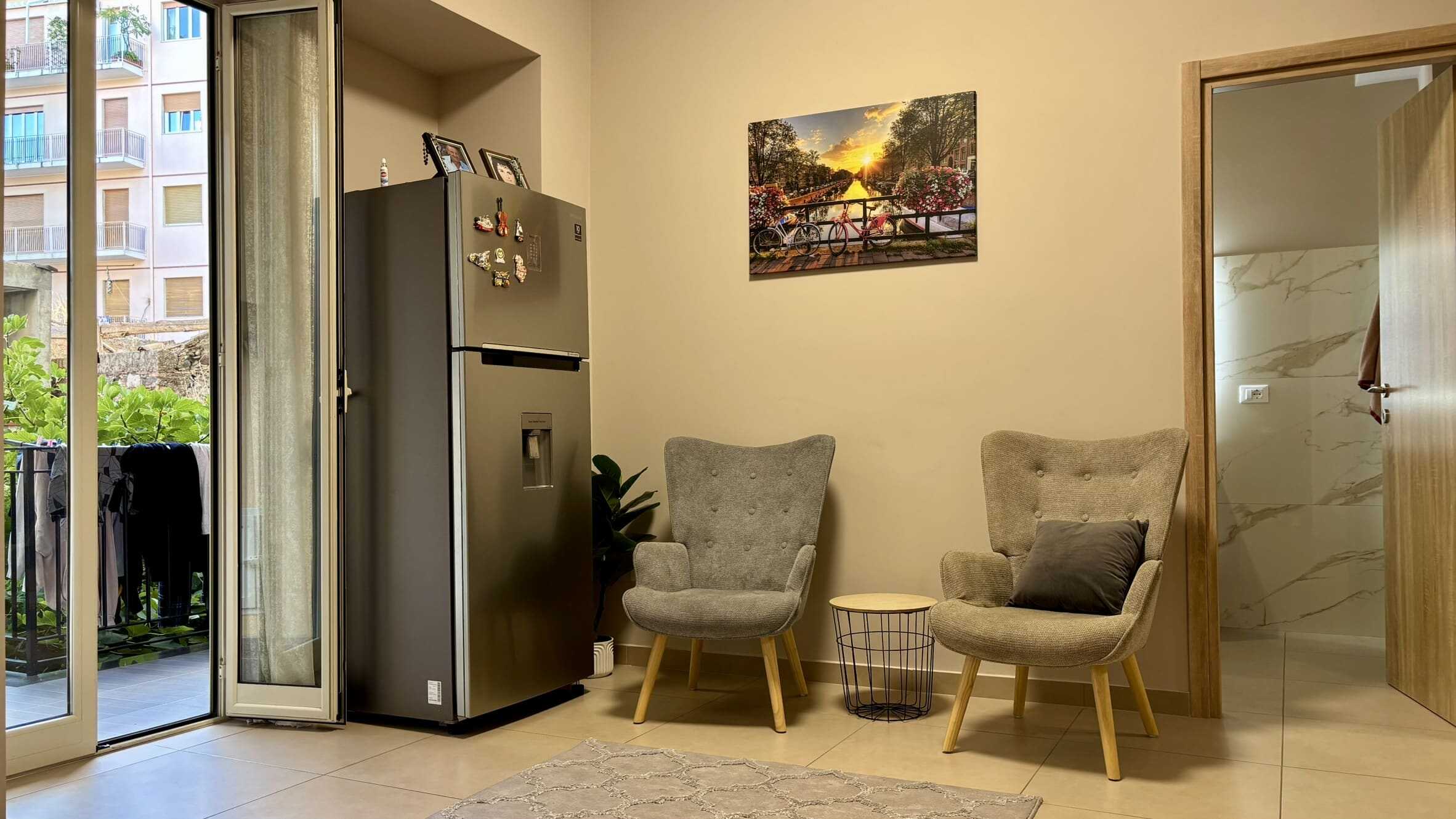 Arredi moderni e confortevoli in soggiorno con balcone, frigorifero con magneti, decorazioni colorate, quadri e piante, atmosfera accogliente e luminosa, ideale per case in vendita o affitto.