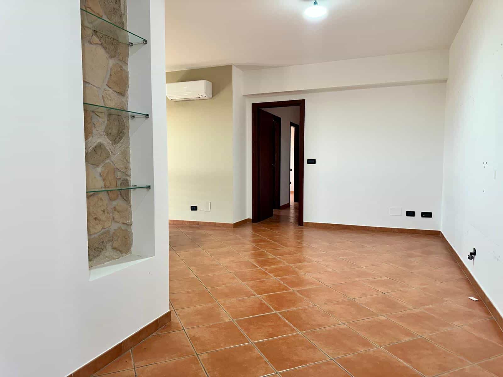Interno di un appartamento vuoto con pareti bianche, pavimento in ceramica e aria condizionata, pronto per arredamento e personalizzazione.