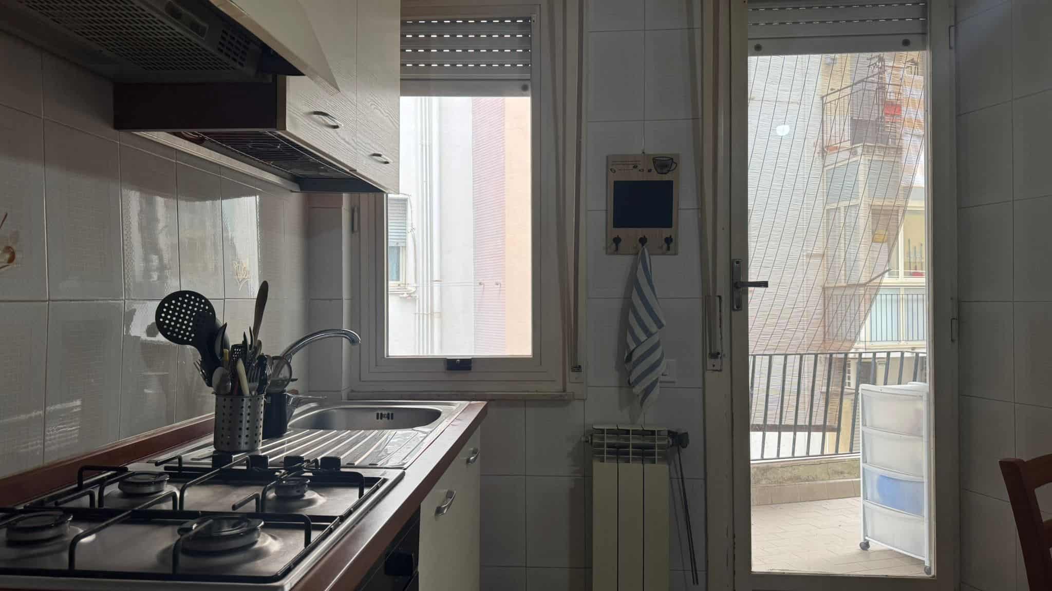 Finestra e porta balcone in cucina con vista su edificio e balcone con scatola porta oggetti, stile semplice e funzionale, ideale per appartamenti moderni, dettagli di arredamento e illuminazione naturale.