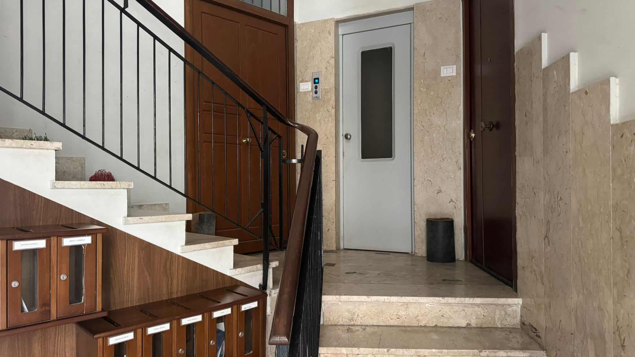 Scarpiera in legno e scale in marmo nell'ingresso di un appartamento. Sistema di sicurezza con ascensore e pareti in marmo beige, ottimo per immobili di lusso e soluzioni abitative moderne.