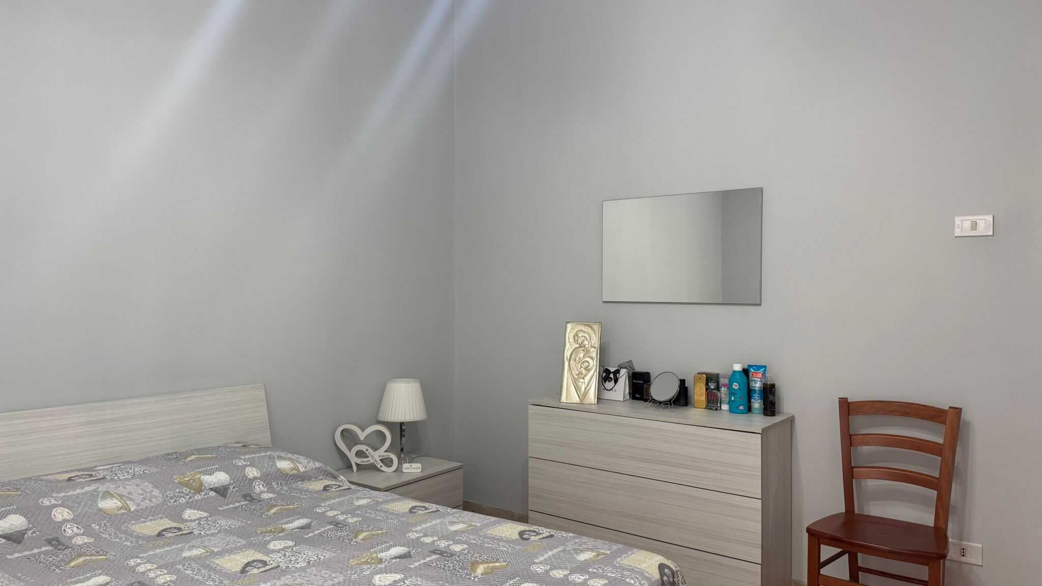 Letto matrimoniale con biancheria coordinata in camera moderna, arredamento minimale e pareti grigie, elemento di stile e comfort, perfetta per immobili di design e soluzioni abitative eleganti.