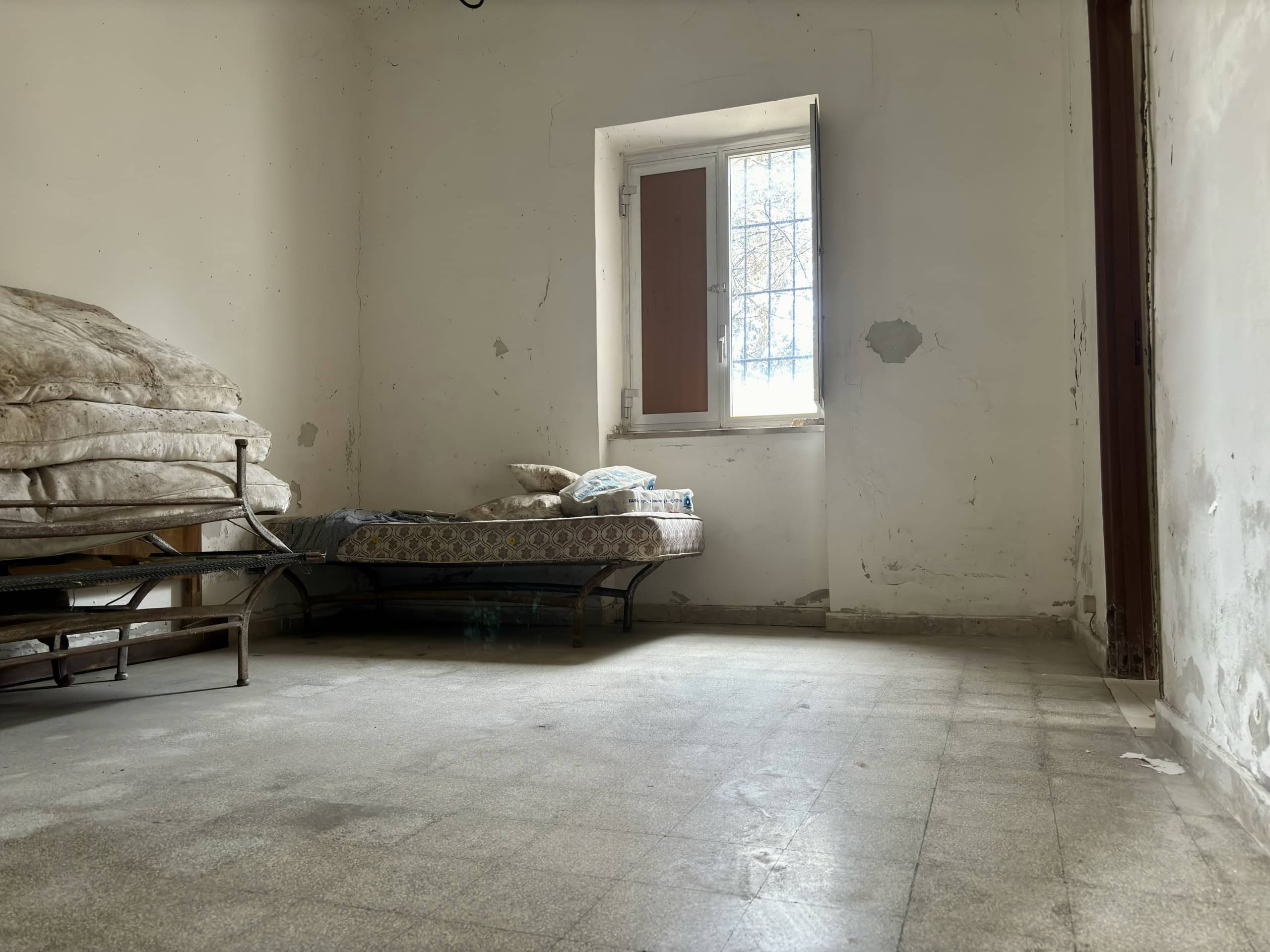 Vecchio appartamento da ristrutturare con pareti in cattivo stato, pavimento in piastrelle e finestra che permette l'ingresso di luce naturale, ideale per progetti di ristrutturazione e interior design.