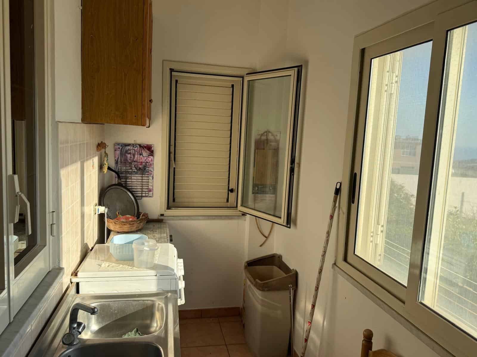 Finestra aperta in cucina con vista sul balcone, spazio domestico luminoso e funzionale, arredo semplice, cucina con lavabo e stoviglie, ambiente tranquillo e ideale per la vita quotidiana.