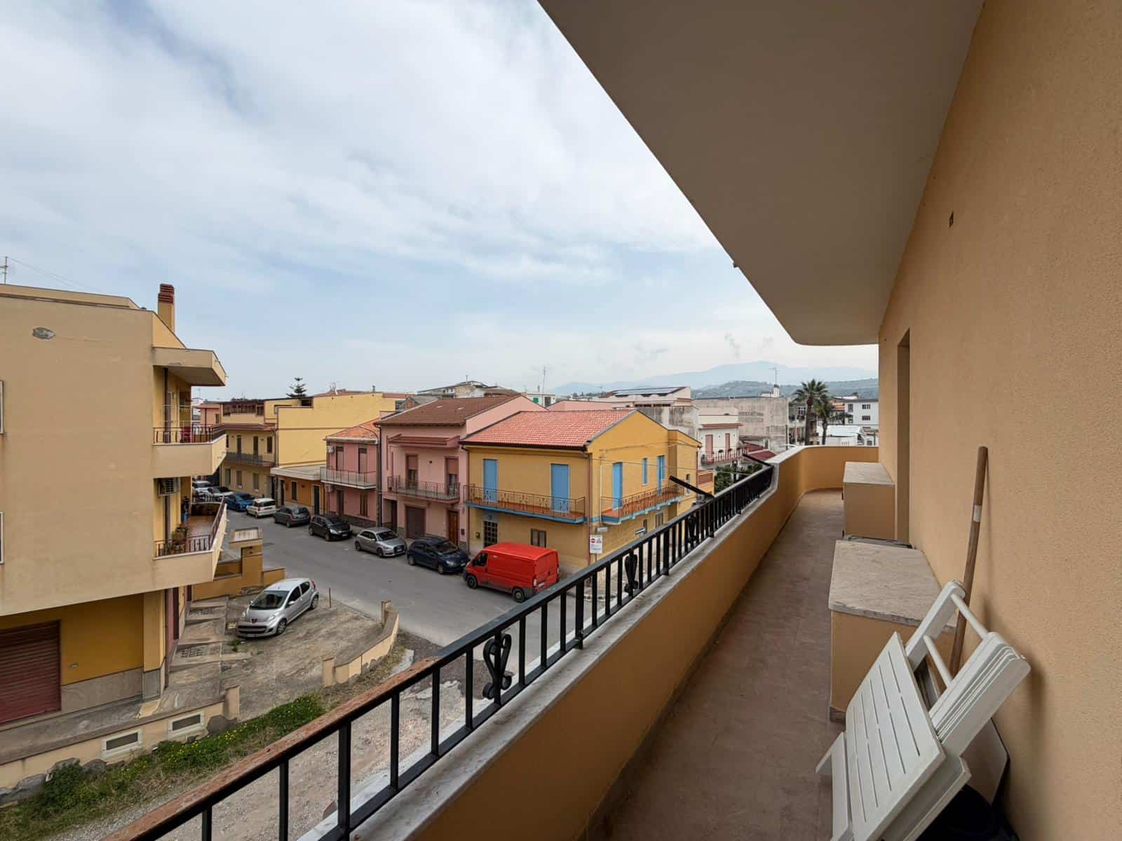 Ampio balcone con vista sul quartiere residenziale di NextCasa, con case colorate e strada trafficata, ideale per rilassarsi all'aperto e godersi il panorama urbano.
