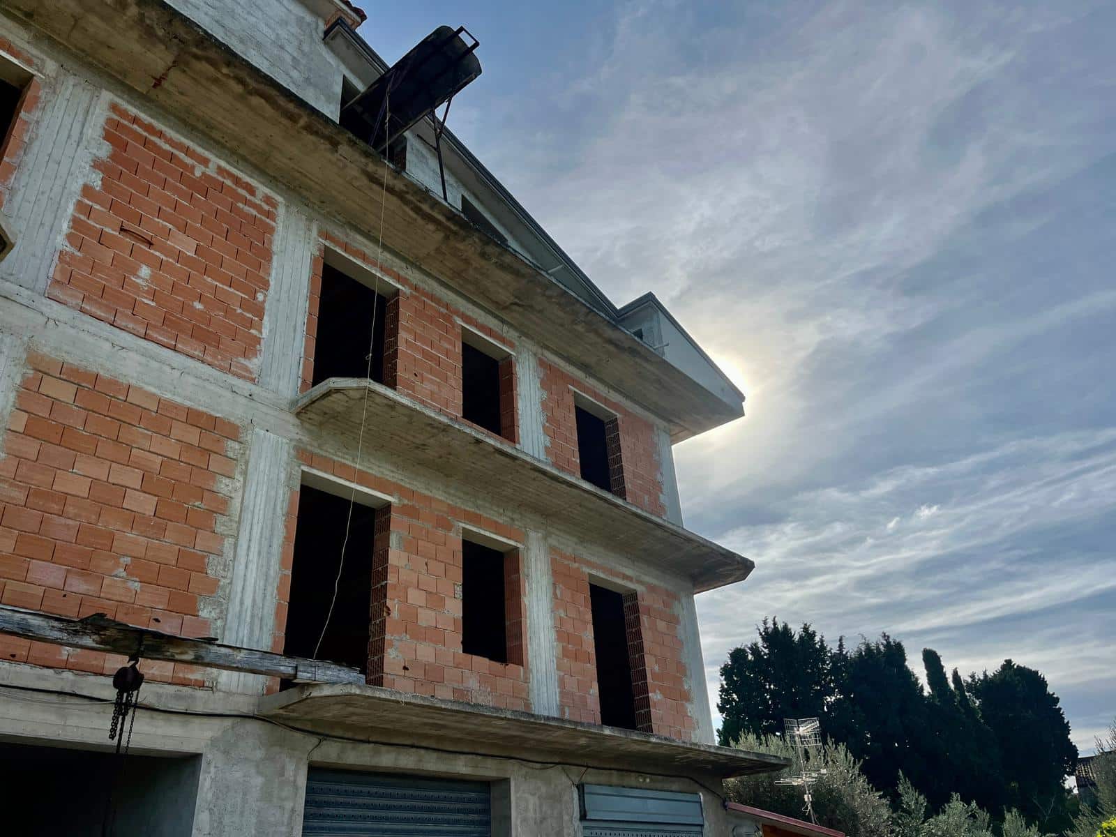 Fase di costruzione di una casa con struttura in mattoni, con balconi e finestre non ancora installate, sotto un cielo nuvoloso, rappresentando lavori di edilizia moderna.