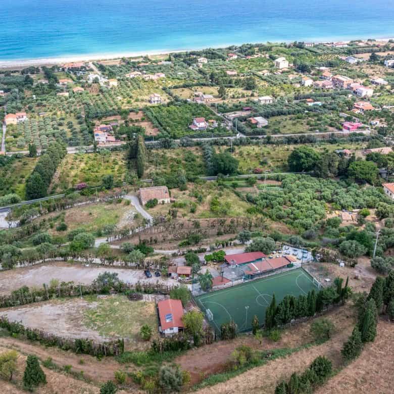 Ampia vista aerea di un complesso residenziale e campi da tennis immersi nel verde, con vista mare sullo sfondo, in una zona tranquilla e naturale della costa italiana.