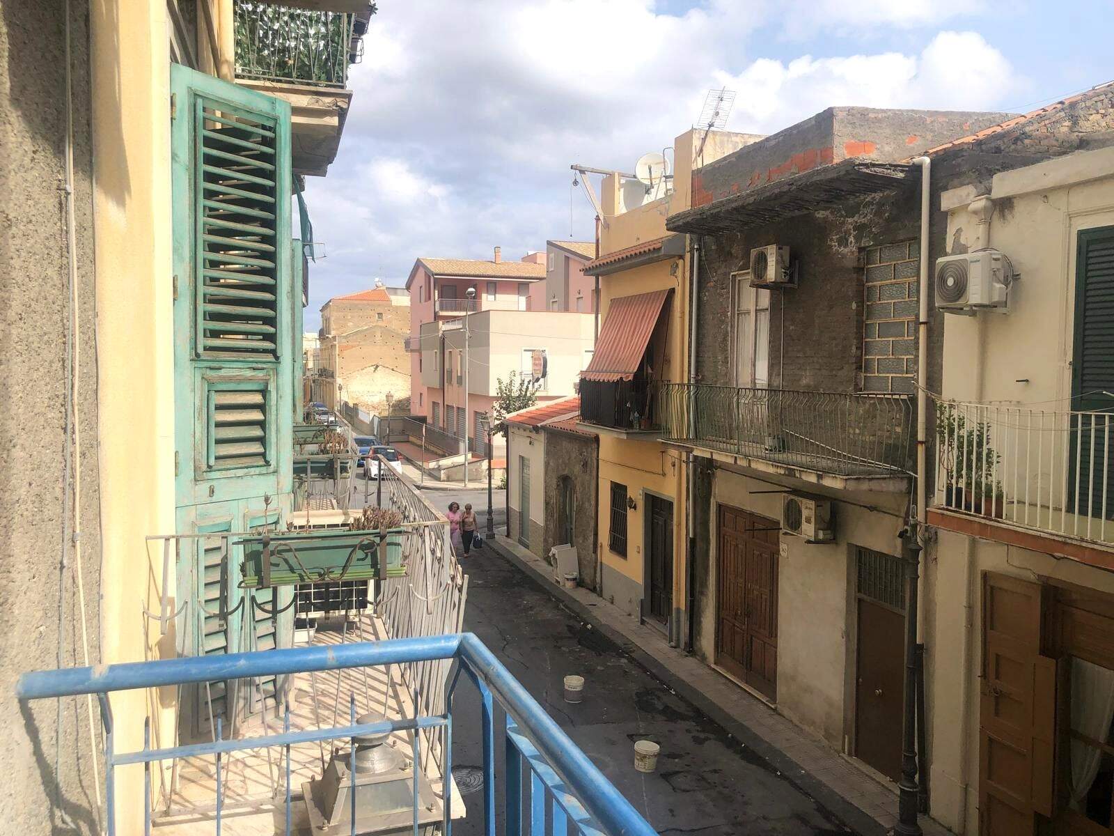 Balcone con vista su strada di un quartiere residenziale, case colorate e abitazioni con aria condizionata, in un tipico scenario urbano italiano.