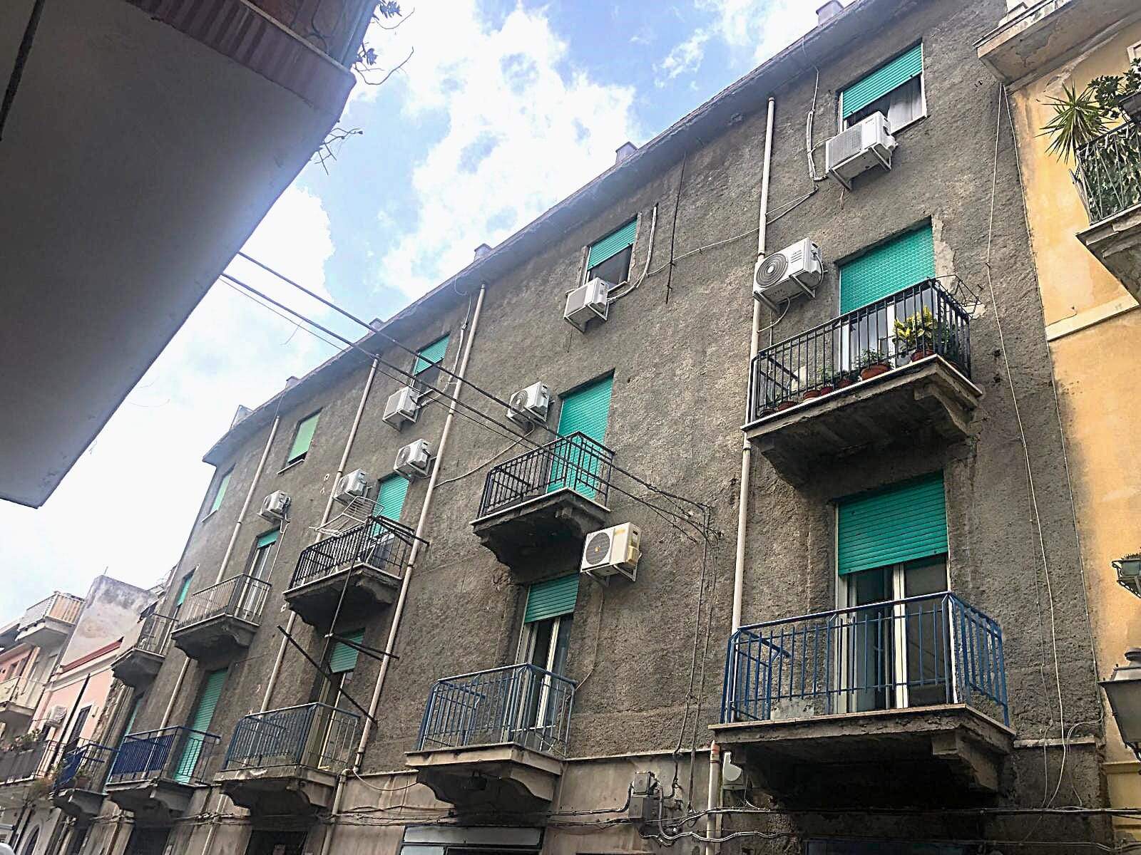 Balconi con ringhiere in metallo e condizionatori su facciata di edificio residenziale in zona urbana, vista dall'angolazione con cielo blu e nuvole, rappresenta immobili per investimento o affitto a Napoli.