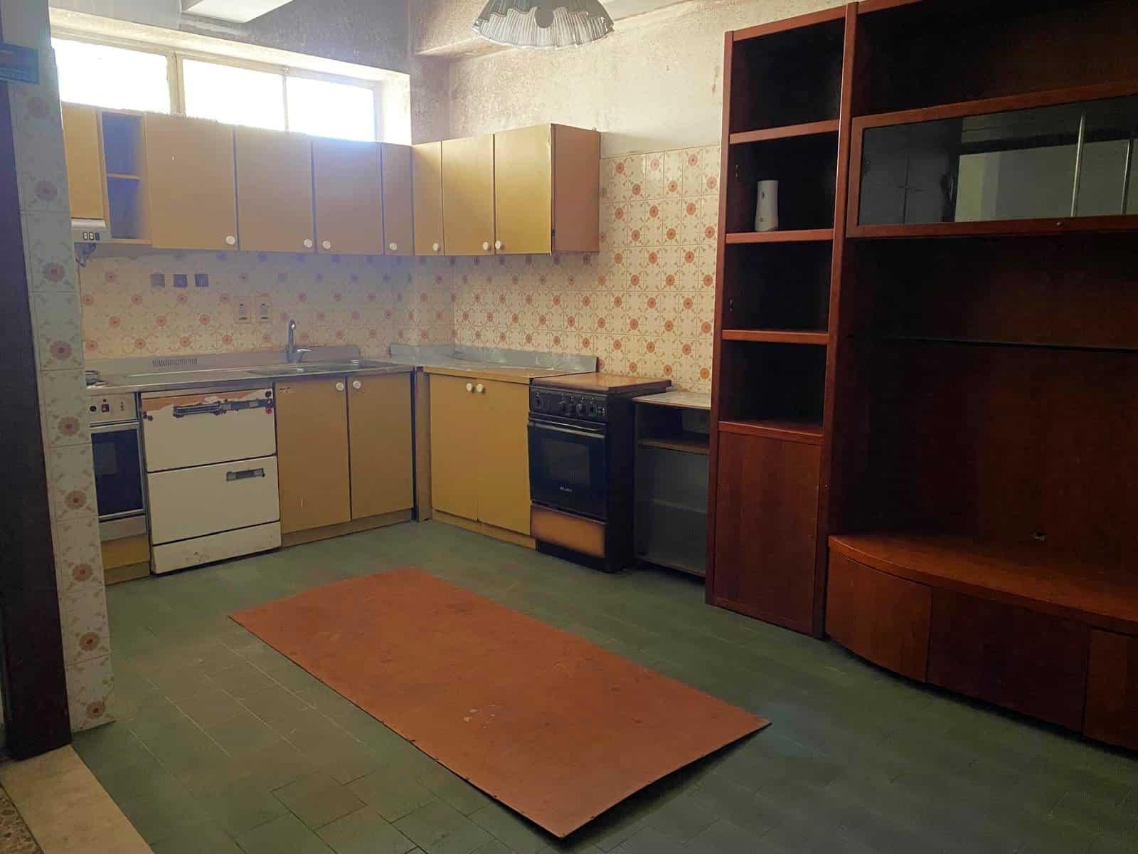 Vecchia cucina arredata con ante gialle, pavimento in piastrelle verdi e pensili in legno massello, perfetta per investimento immobiliare o ristrutturazione in zona centrale.