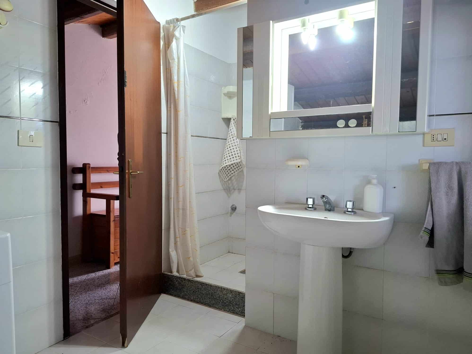 Lavabo bianco con specchio e finestra in bagno, arredi semplici e funzionali, illuminazione efficace, adatto per case o appartamenti, ambienti ristrutturati e pratici.