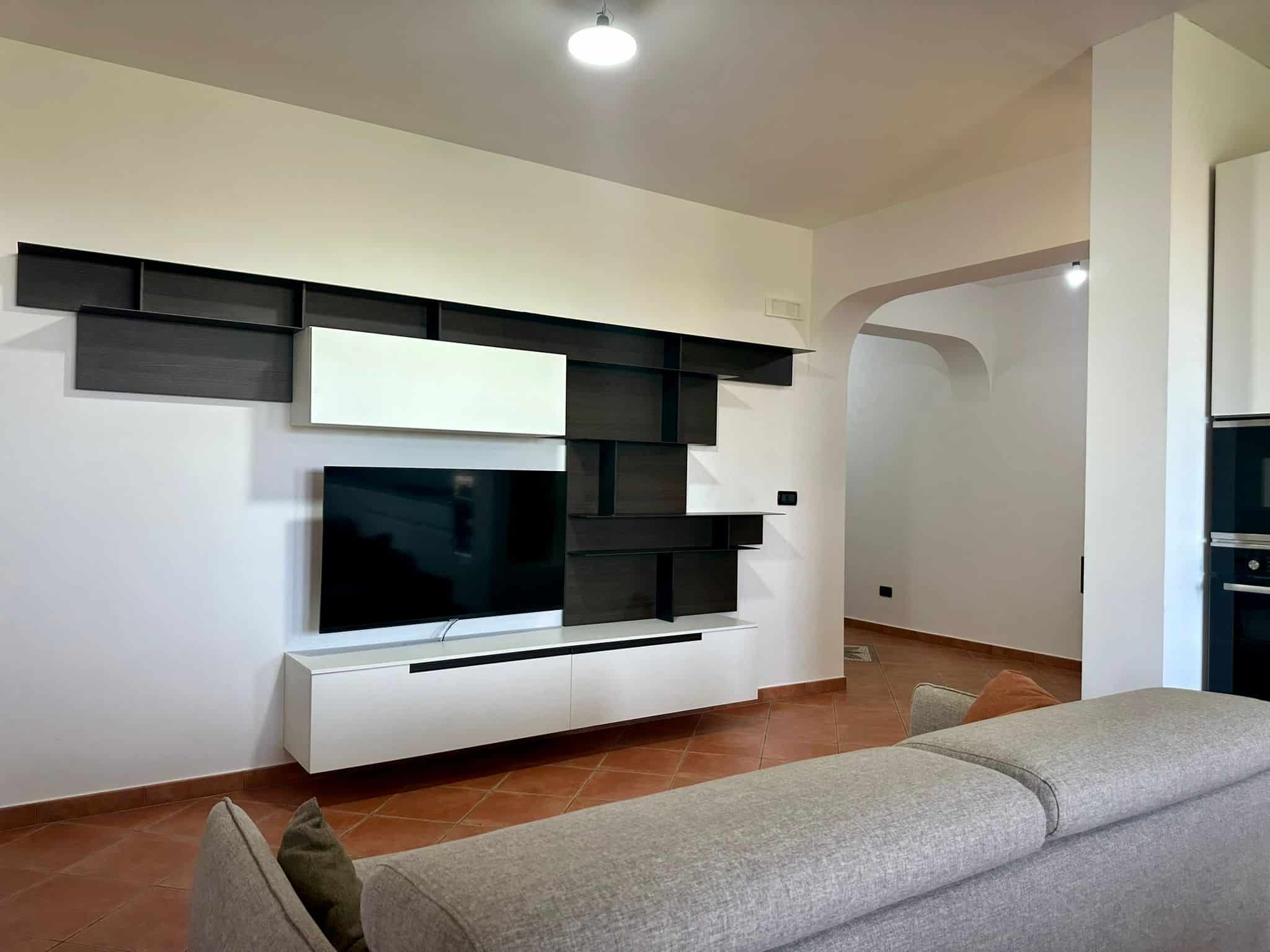 Schermo TV e mobile porta TV bianco con mensole nere in soggiorno, arredamento moderno, ambiente luminoso, stile minimalista, centro living, casa elegante.