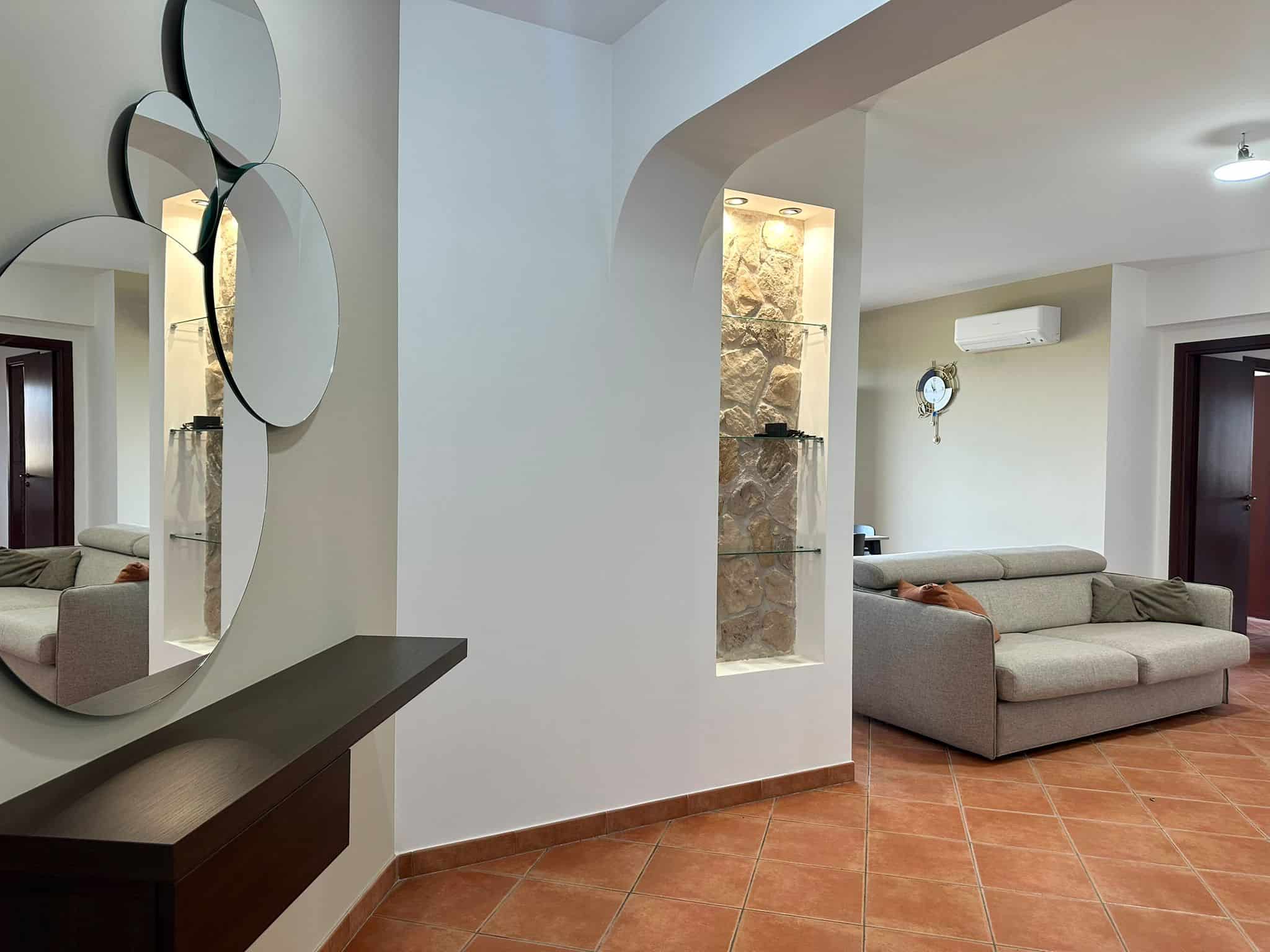 Elegante soggiorno con divano beige e parete in pietra, arredamento moderno, clima e orologio decorativo,perfetto per vivere in ambienti accoglienti e di design.