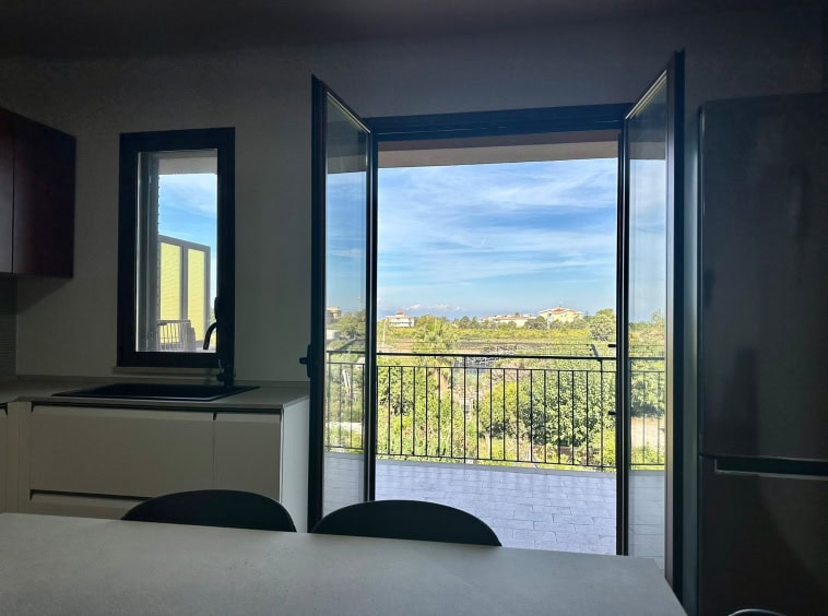 Balcone con vista panoramica su area verde e cielo sereno, accessibile dalla cucina moderna, ambiente luminoso e accogliente, ideale per godersi la natura e il comfort domestico.