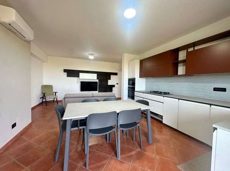 Moderno soggiorno con cucina a vista, mobili minimalisti, area pranzo con tavolo e sedie, parete TV decorativa, dettagli di design, soluzione abitativa funzionale e contemporanea.