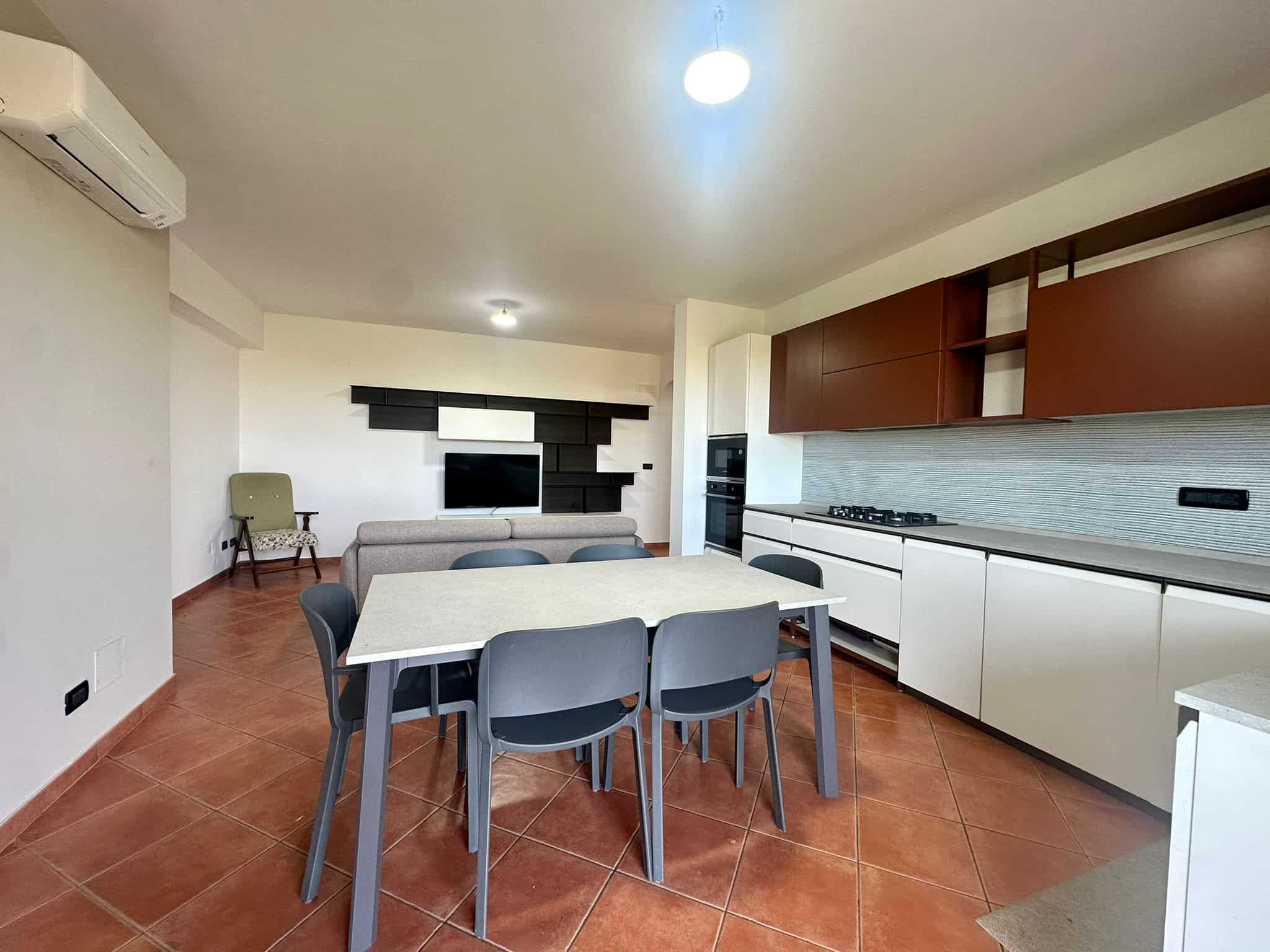 Moderno soggiorno con cucina a vista, mobili minimalisti, area pranzo con tavolo e sedie, parete TV decorativa, dettagli di design, soluzione abitativa funzionale e contemporanea.