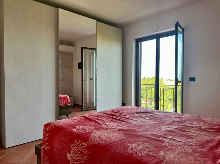 Elegantè camera da letto con grande finestra e balcone con vista su aree verdi, arredamento moderno e comfort abitativo, ideale per residenze di qualità.