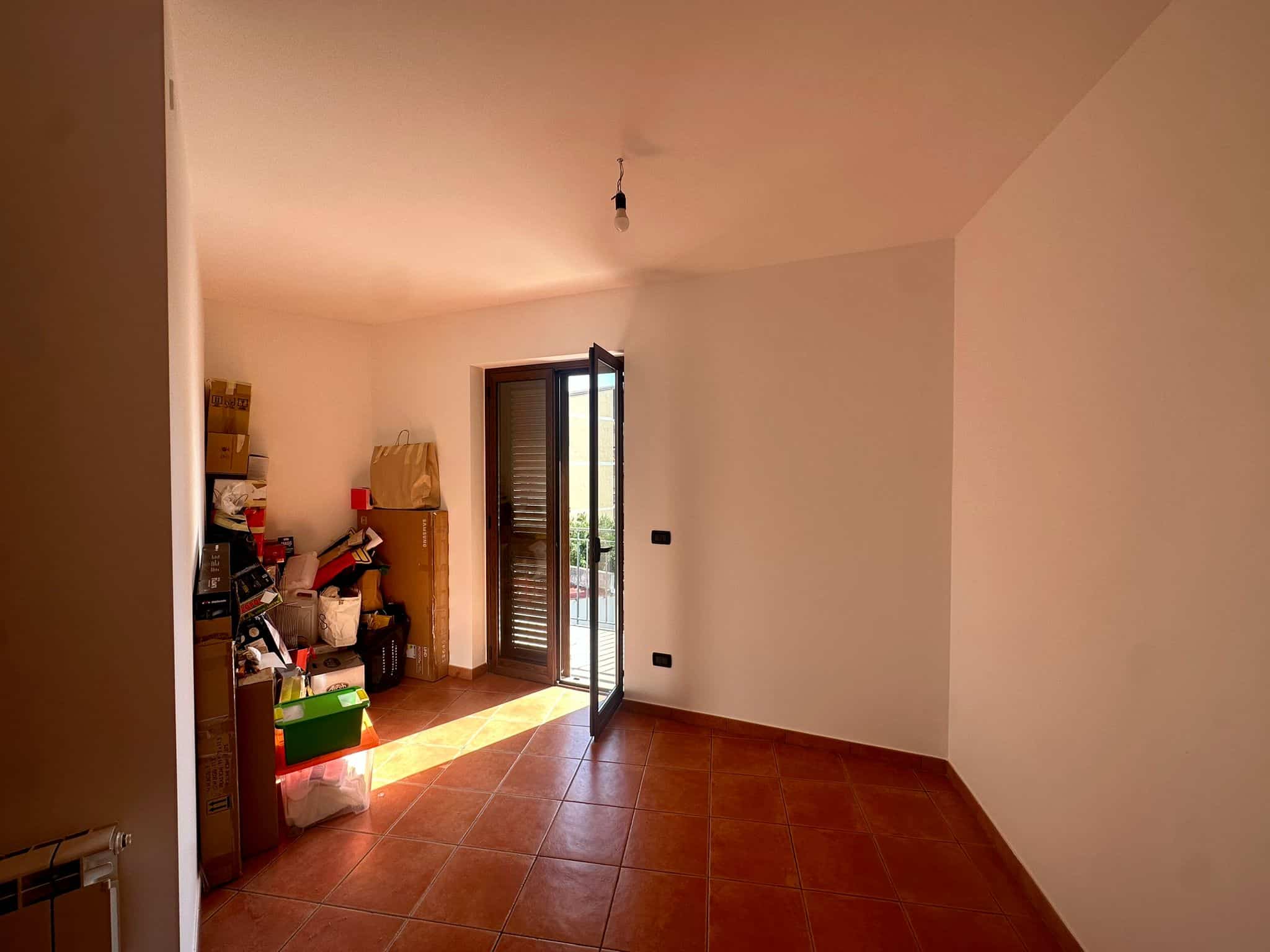 Ampio soggiorno vuoto con porta finestra che dà su un balcone, pavimento in ceramica e pareti bianche, ideale per rinnovare e arredare secondo il proprio stile, pronto per essere personalizzato.