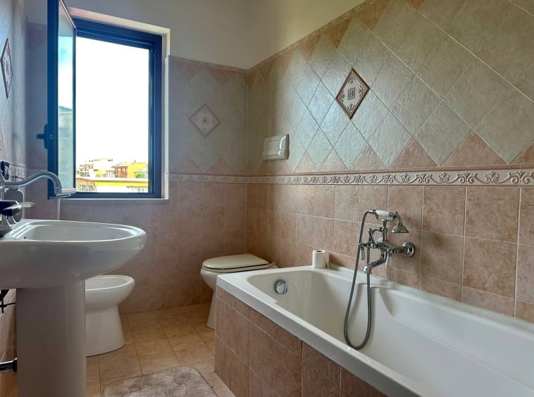 Lavabo e vasca da bagno in un bagno luminoso con piastrelle beige e finestre panoramiche in un appartamento NextCasa.