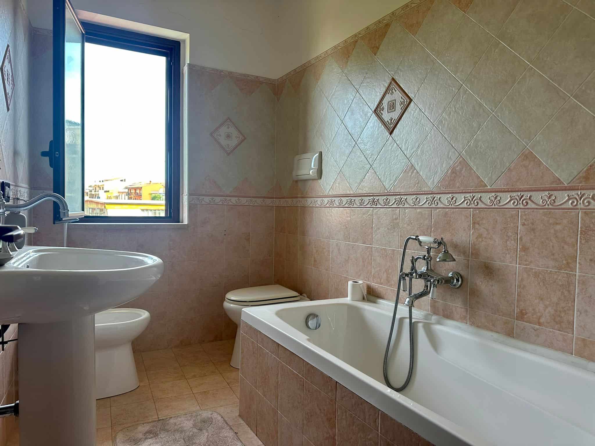 Lavabo e vasca da bagno in un bagno luminoso con piastrelle beige e finestre panoramiche in un appartamento NextCasa.