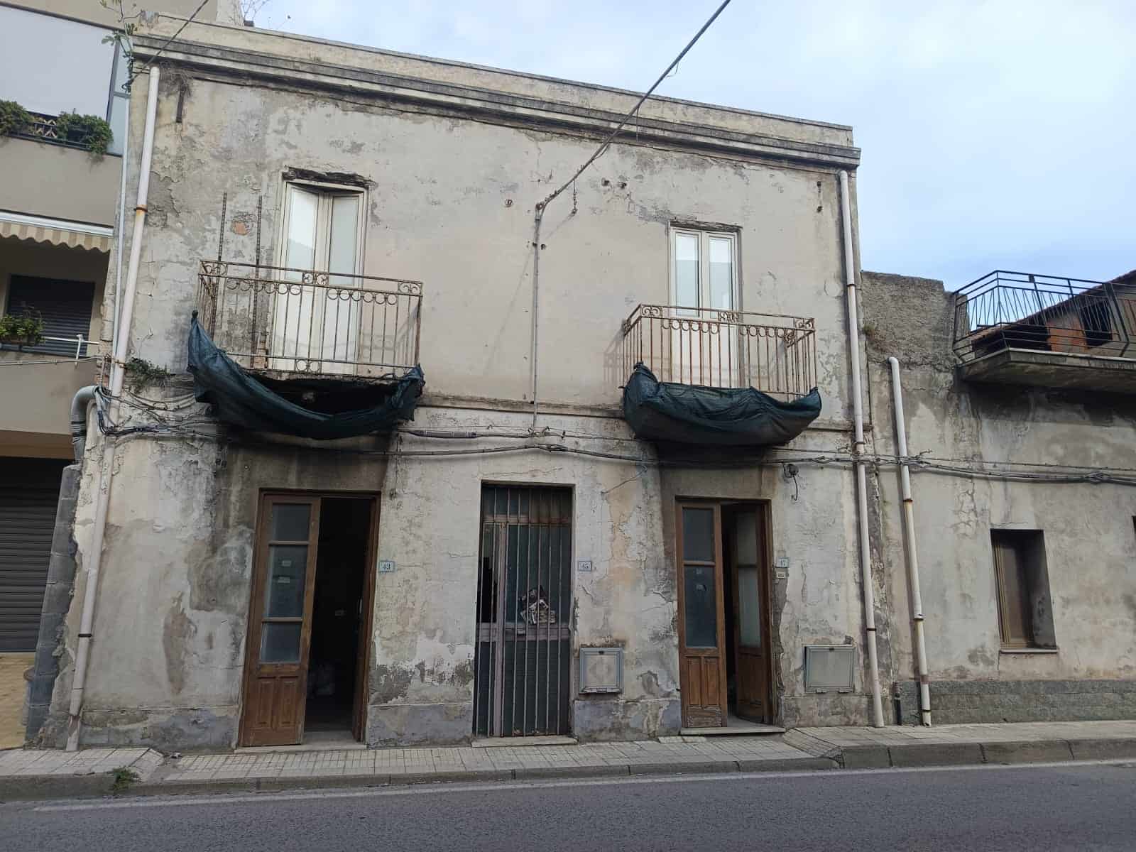 Vecchio edificio residenziale da ristrutturare con balconi e porte in legno, facciata usurata e comodo accesso stradale, ideale per realizzare una moderna abitazione o investimento immobiliare.