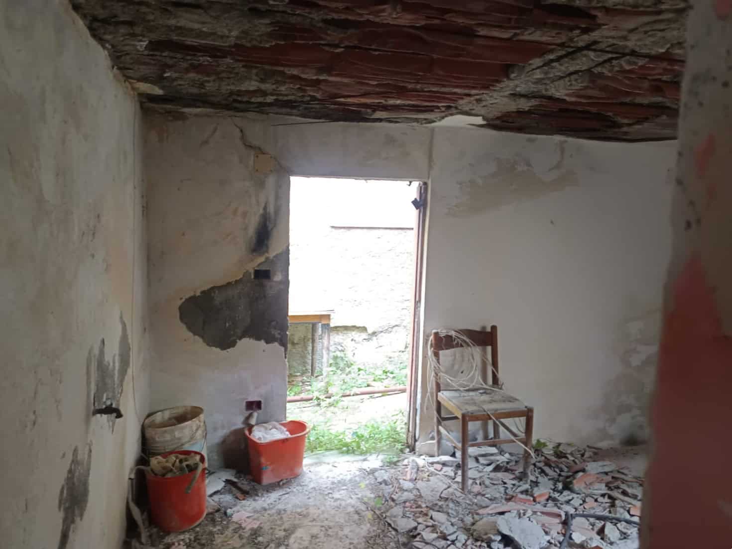 Vecchio ambiente in ristrutturazione, pareti danneggiate e pavimento in rovina, ingresso aperto con vista su giardino, lavori di edilizia e restauro in corso nel immobile NextCasa.