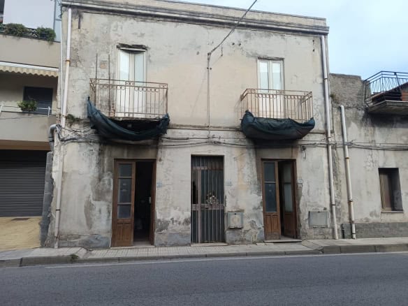 Vecchio edificio residenziale in stato di abbandono con balconi e porte in legno, pareti rovinate e finestre senza persiane, situato lungo strada urbana in area urbana.