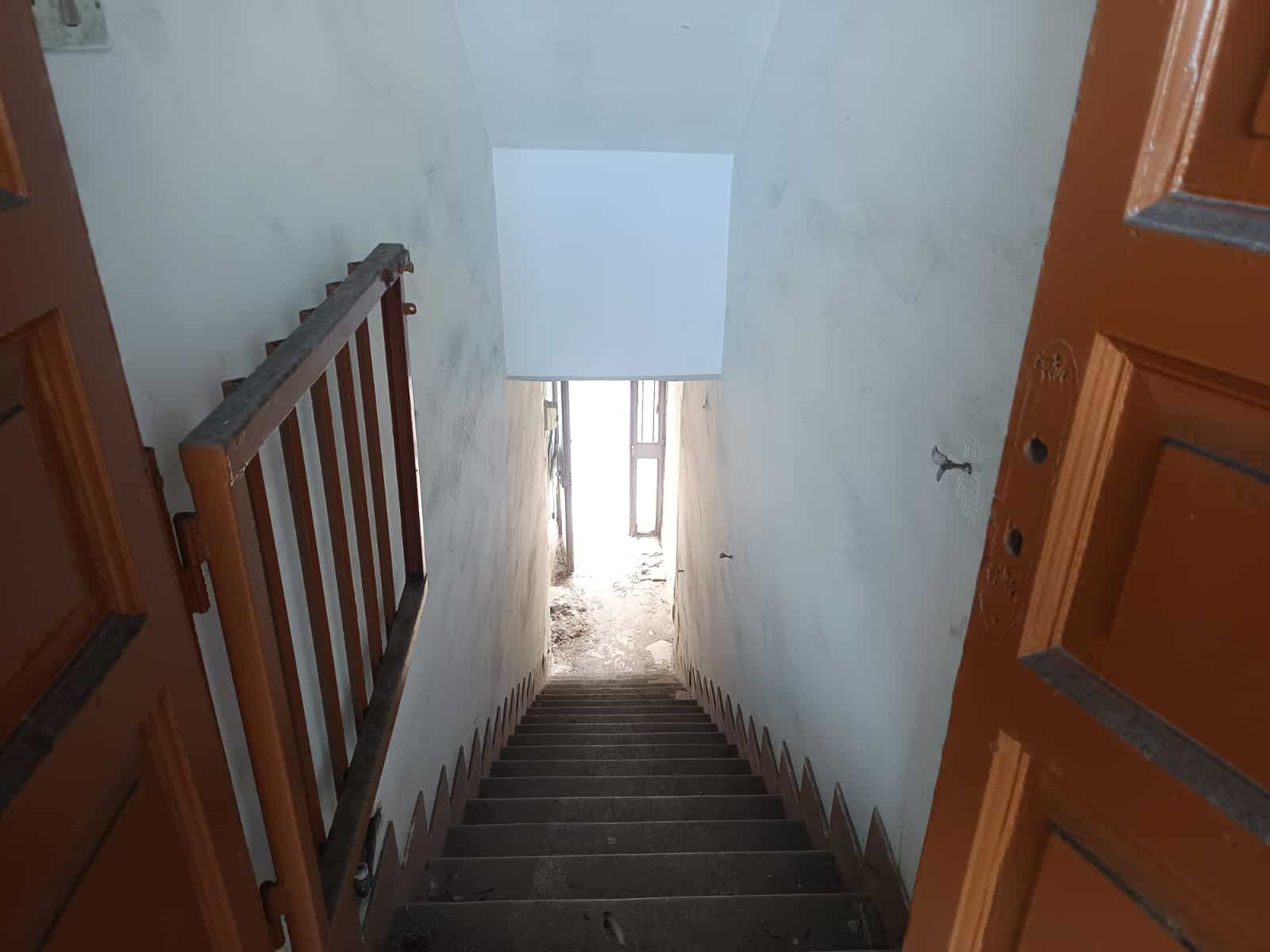 Scala interna in fase di ristrutturazione, vista dall'alto, con ringhiera in metallo e gradini in cemento, luce naturale proveniente da finestra.