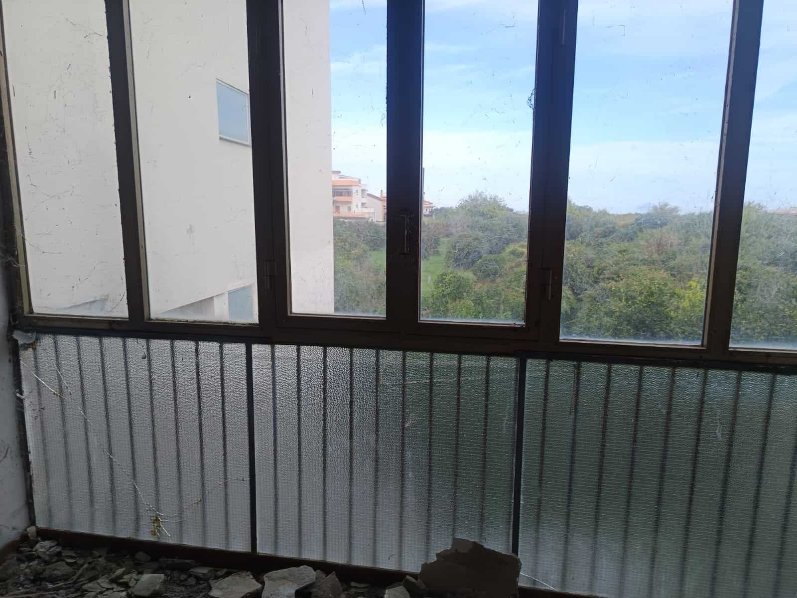 Finestre con infissi in alluminio e vetri panoramici, vista su natura e quartieri residenziali, ambiente luminoso e ventilato, ideale per ambienti da ristrutturare o rinnovare.