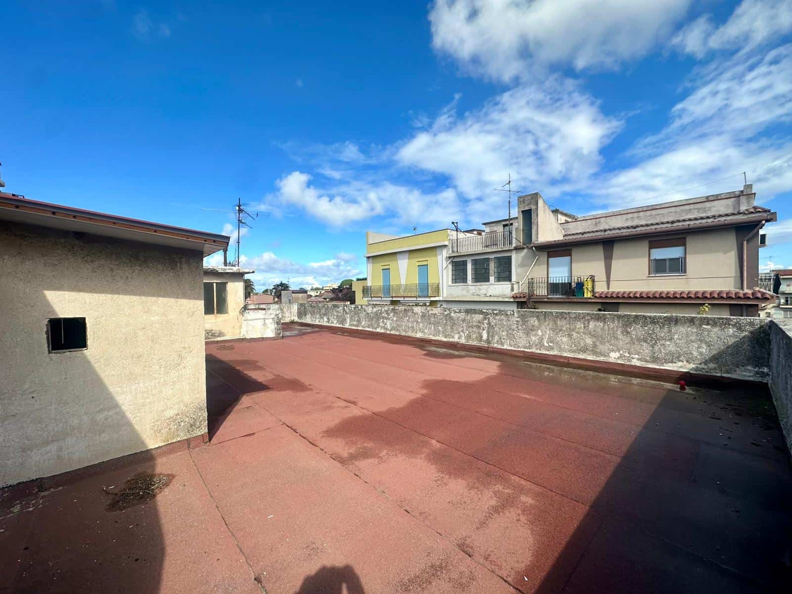 Tetto terrazza con vista sulla città, spazio ampio e soleggiato con superficie in vinile rosso, ideale per relax e soggiorno all'aperto, vicino a edifici residenziali.
