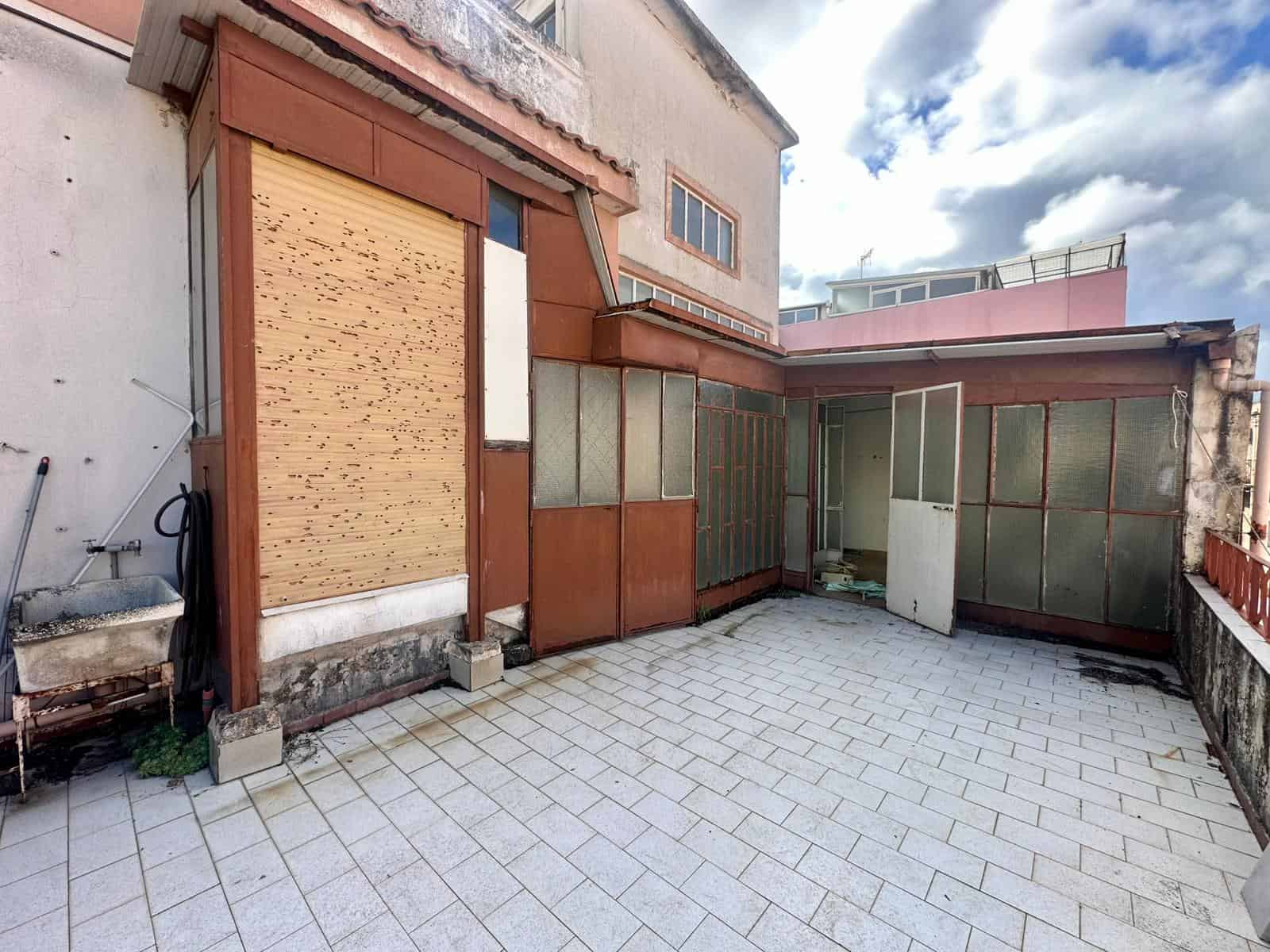 Balcone all'aperto con pavimentazione in piastrelle, in un edificio abitativo, con struttura in metallo e vetro, area spaziosa per relax e giardinaggio, luce naturale e vista sulla città.