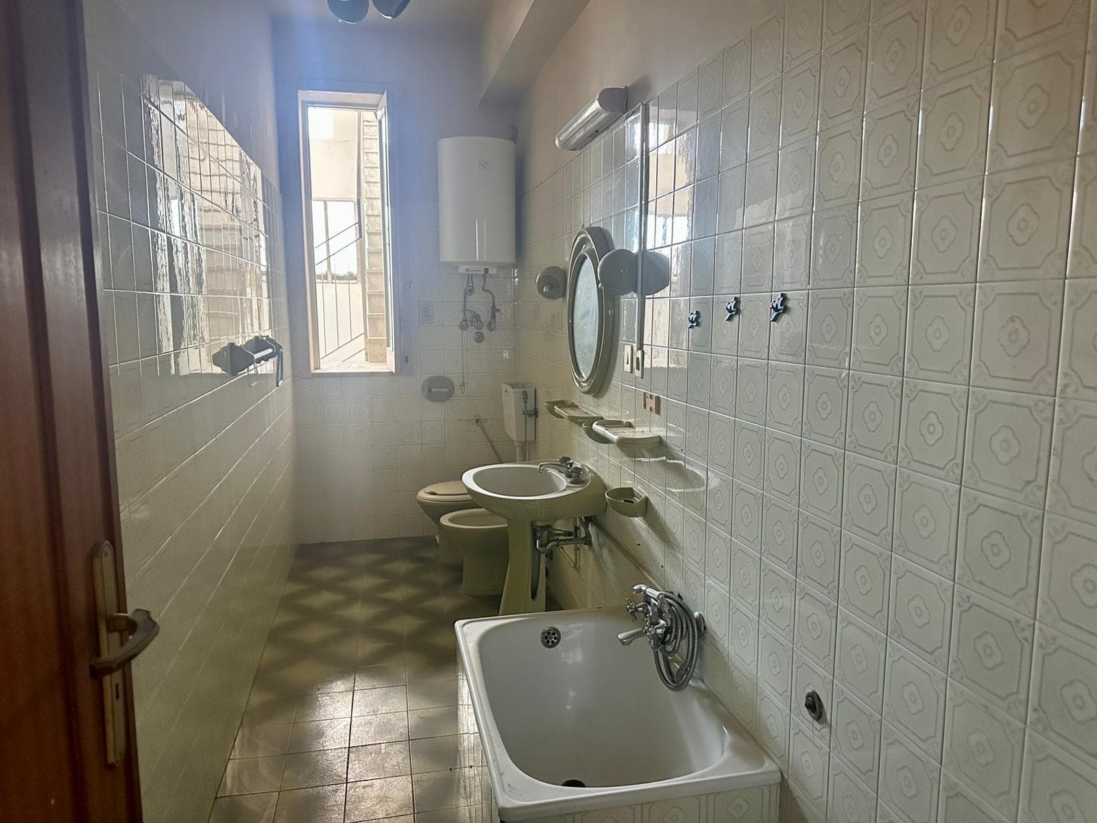 Bagno con vasca e lavabo, finestra e sanitari in stile vintage, piastrelle bianche con motivo geometrico, ambiente luminoso e arioso, ideale per ristrutturazione e design di interni, NextCasa, immobiliare, proprietà in vendita, affitto.