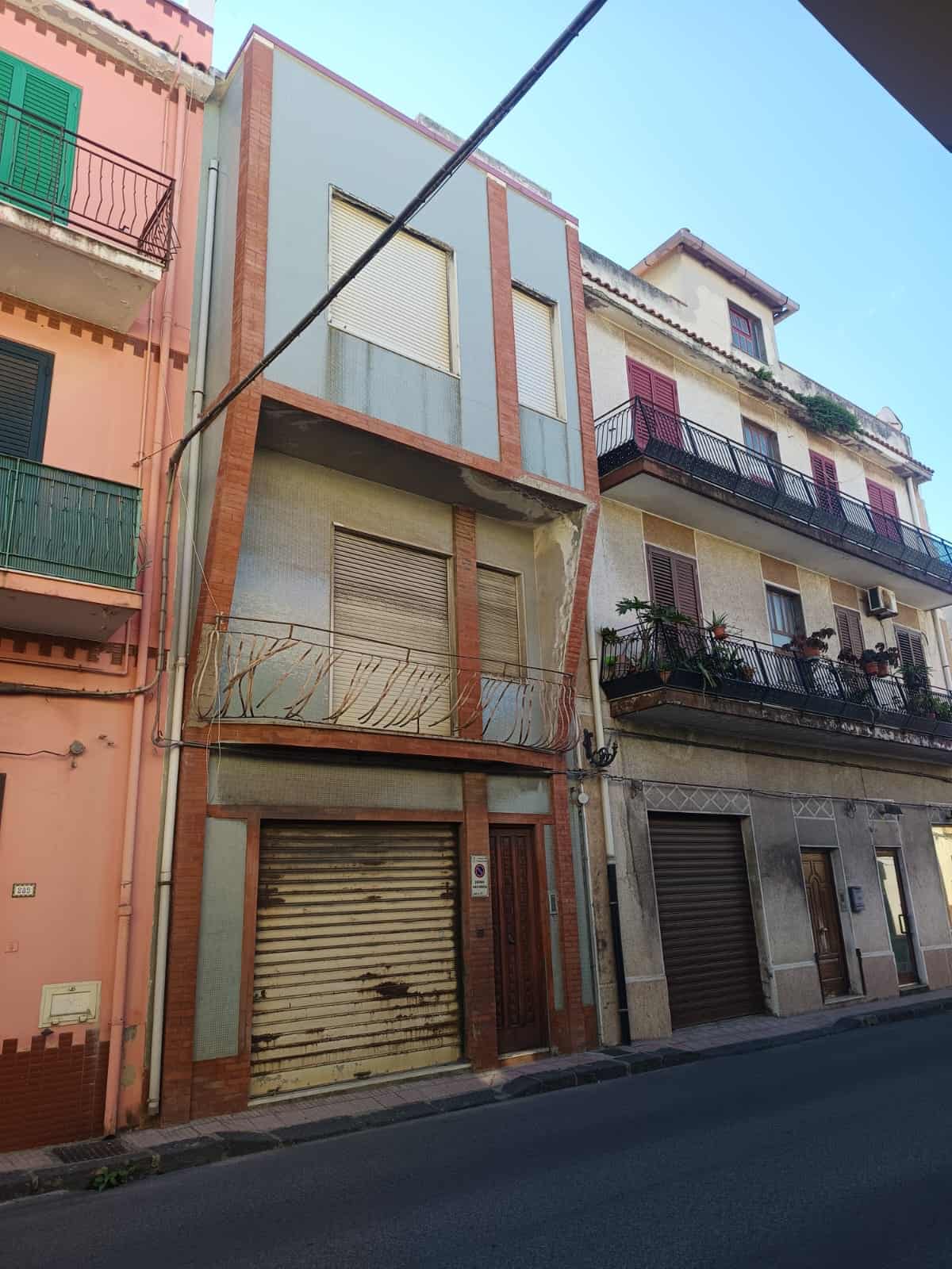 Magazzino in centro città, edificio residenziale con ampio garage e accesso in strada, caratterizzato da strutture in pietra e cemento, situato tra altre proprietà di appartamenti.