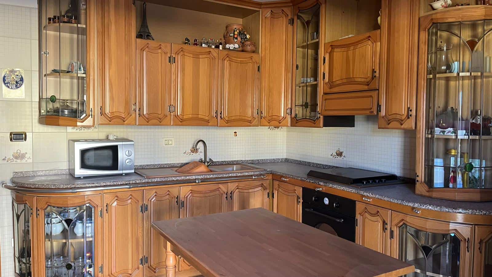 Miccheta cucina in legno con pensili e vetrine, piano cottura e forno integrato, dettagli di arredamento tradizionale, ideale per case in stile classico e rustic chic.