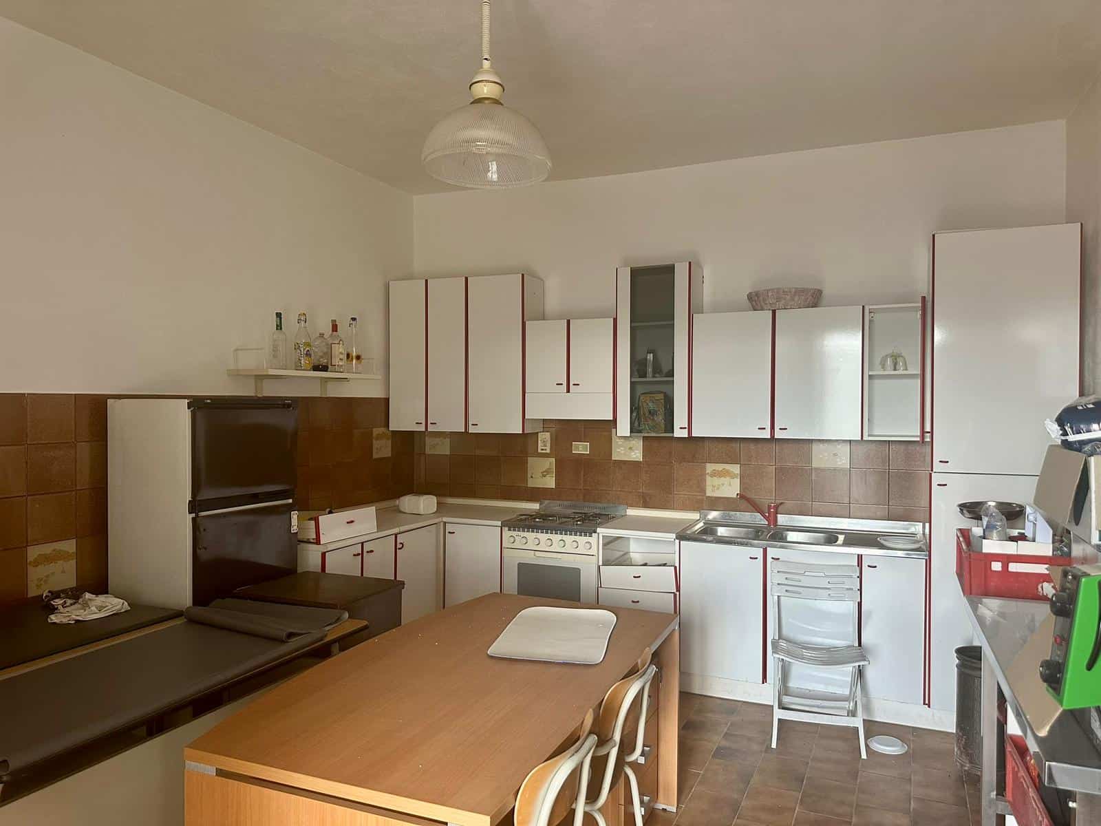 Cucina compatta con mobili bianchi e dettagli rossi, forno, piano cottura e lavabo, ideale per case e appartamenti moderni, con un'atmosfera accogliente e funzionale.