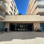 Immagine di un ingresso di un edificio residenziale moderno con facciata in tonalità chiare, ampie vetrate e un'area di parcheggio per scooter e biciclette, in un contesto urbano di villetta o condominio.