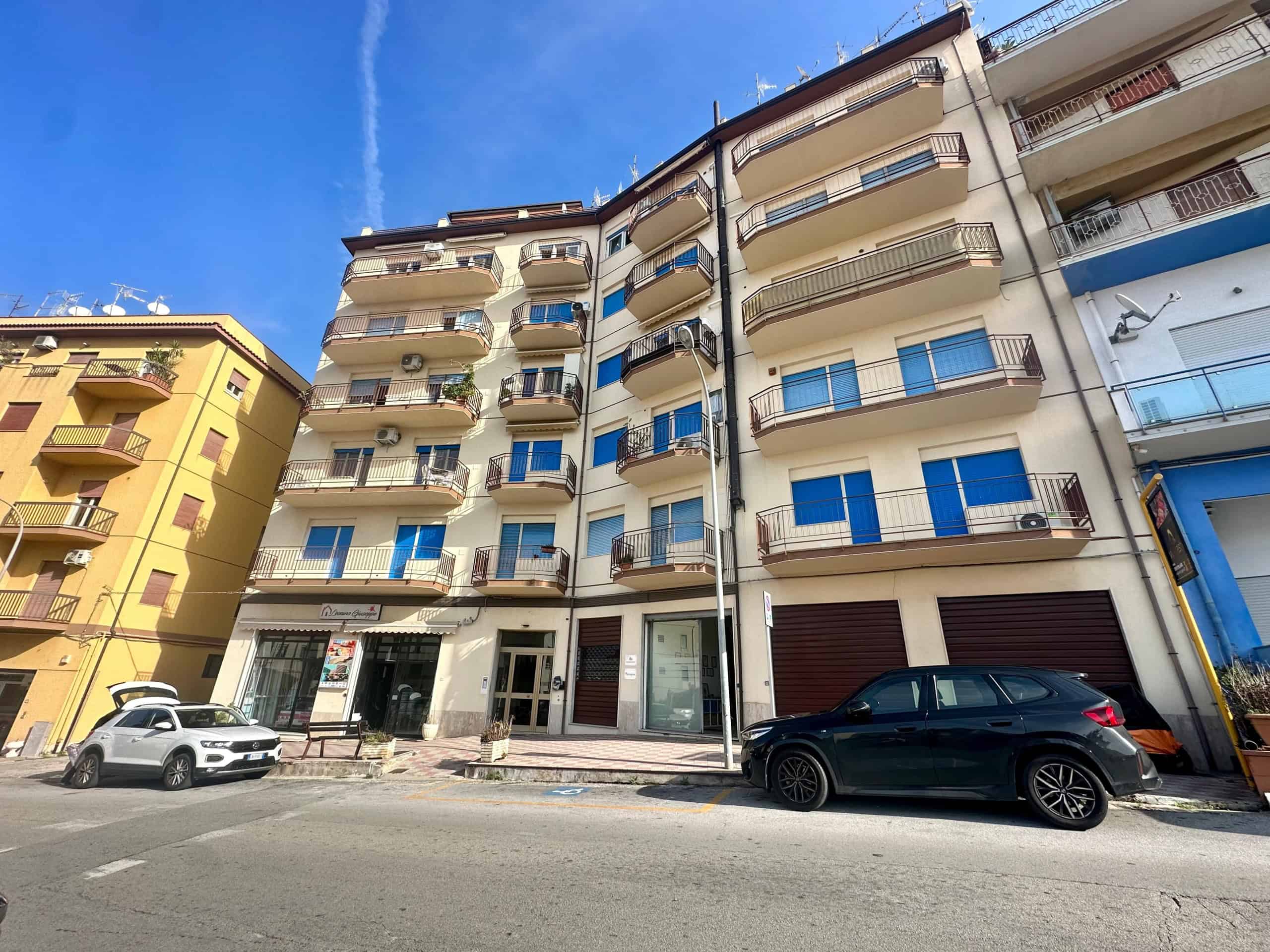 Appartamenti con balconi e negozio al piano terra in zona residenziale a Napoli, edificio moderno e ben mantenuto, parcheggio auto e atmosfera urbana.