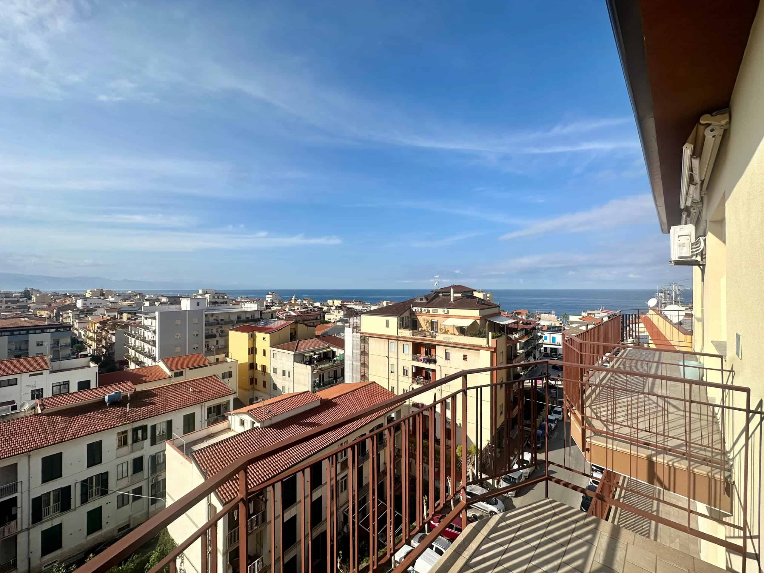 Vista mare e città dalla terrazza di un appartamento a Napoli, con edifici residenziali, tetti rossi e cielo azzurro.