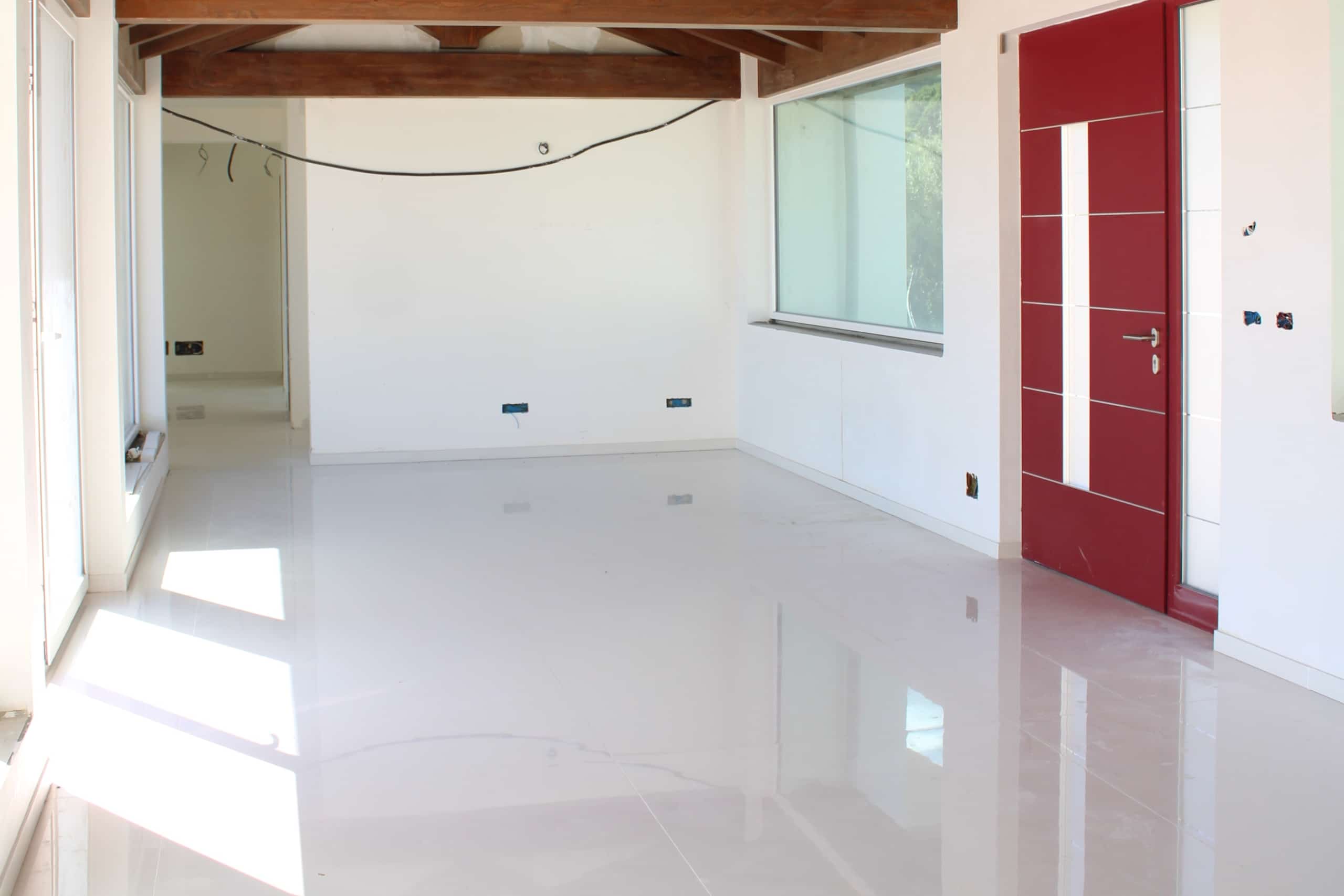 Finestre grandi e porta moderna rossa in un soggiorno nuovo, luminoso e spazioso, pronto per arredare, con pareti bianche e pavimento lucido, ideale per soluzioni di design contemporaneo.