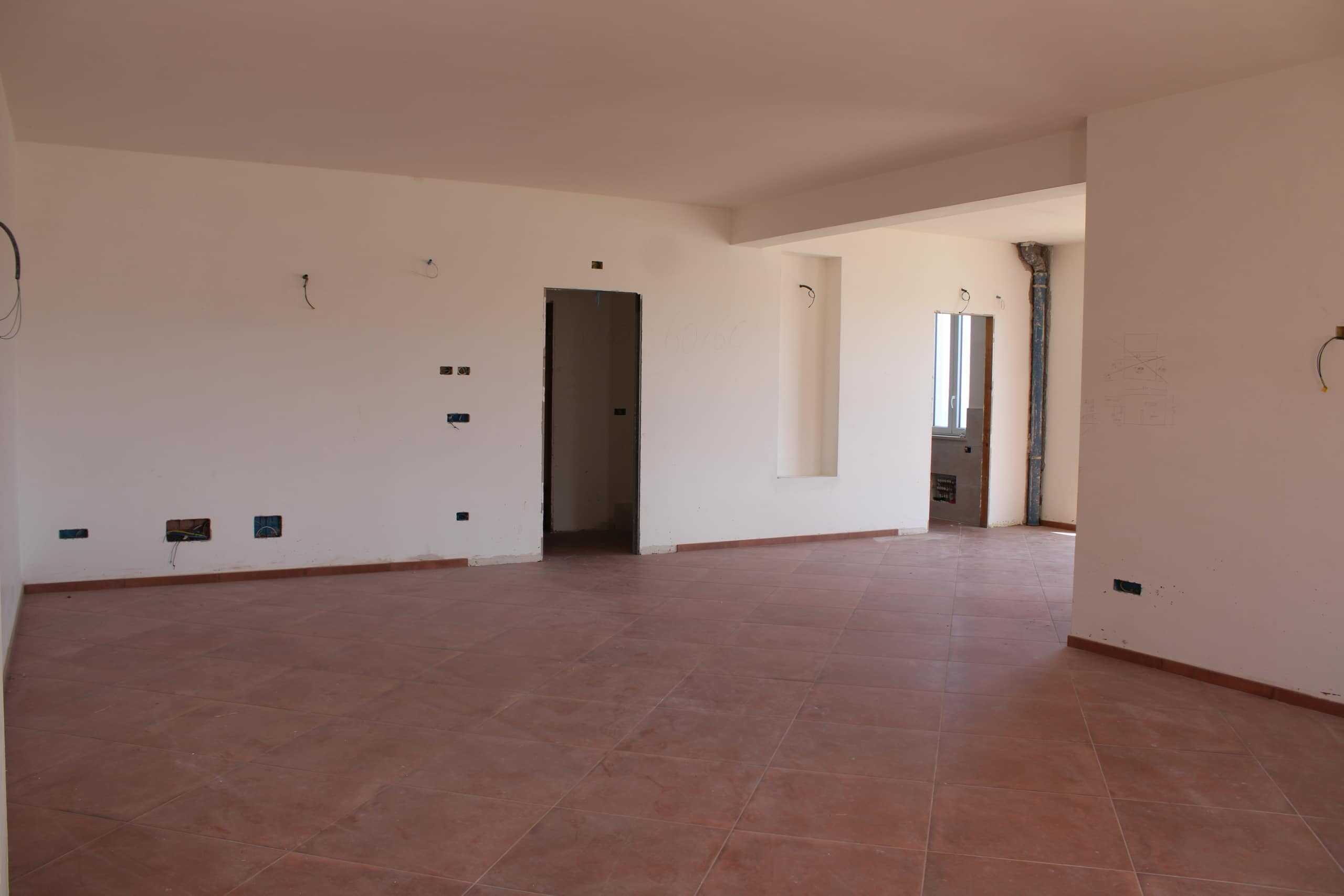 Interni di un appartamento in costruzione o ristrutturazione, con pareti bianche, porta aperta e pavimento in piastrelle di terracotta, pronta per finiture e arredamento.
