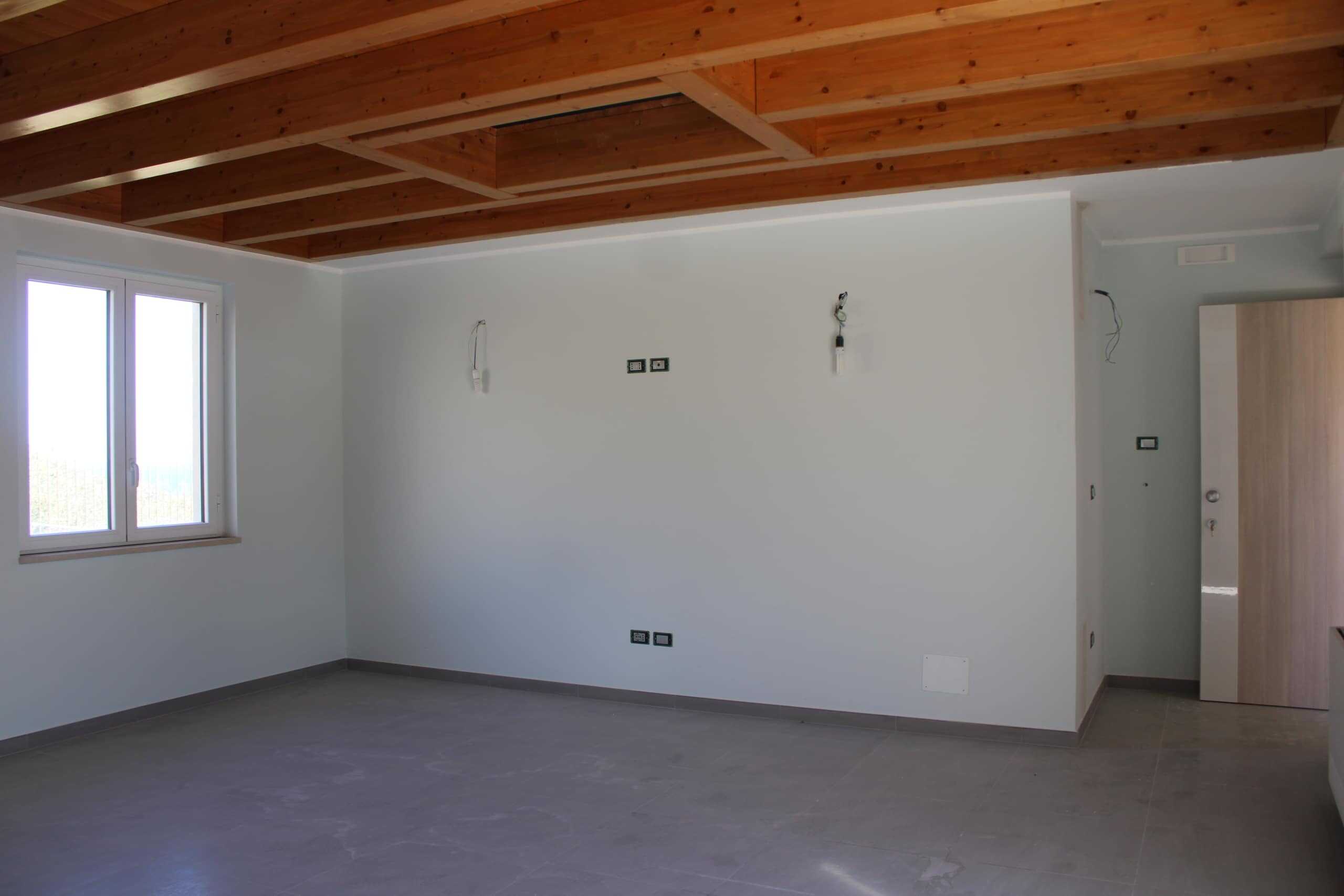 Finestra moderna in un appartamento in costruzione, pareti bianche e soffitto in legno, ambiente luminoso e spazioso, pronto per essere rifinito e arredato.