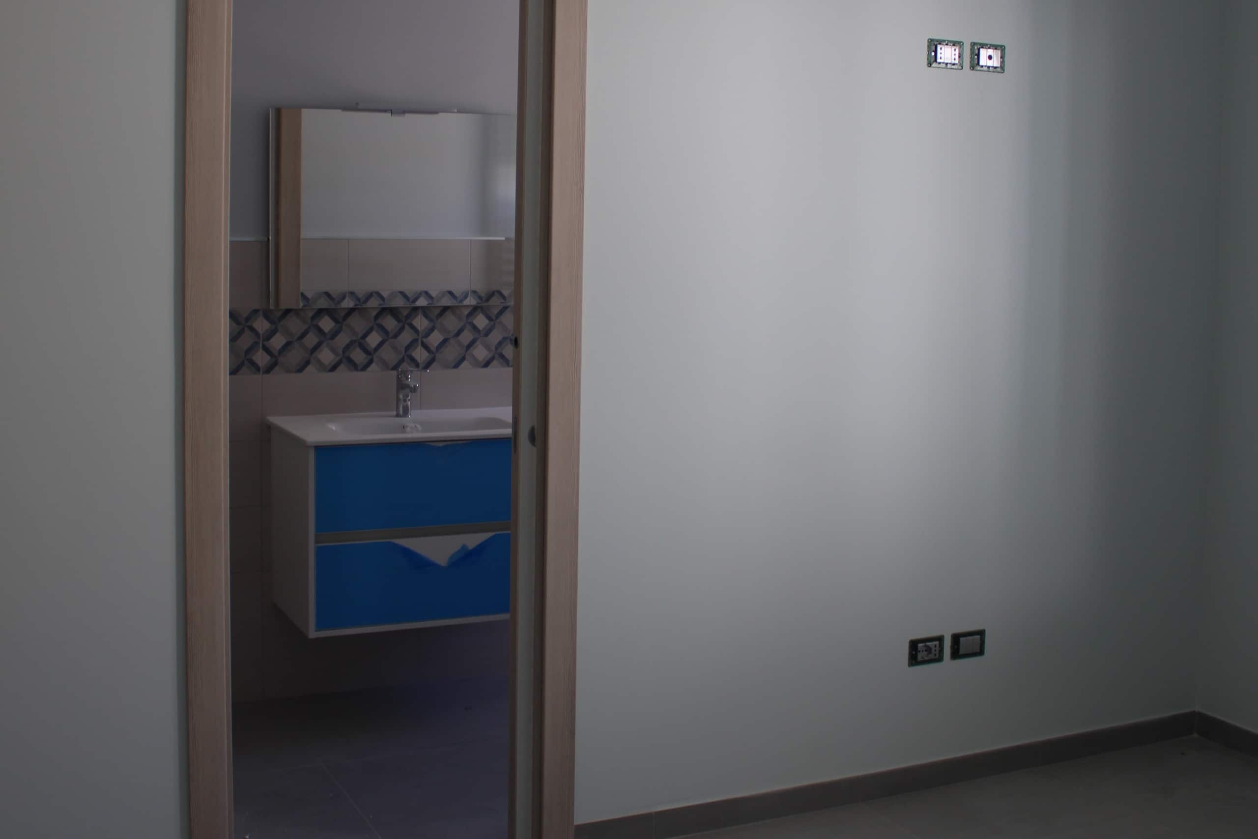 Elevato a bagno con mobiletto blu e lavabo, visibile attraverso una porta aperta, stile moderno e funzionale, ideale per spazi abitativi contemporanei, dettagli di design minimalista.