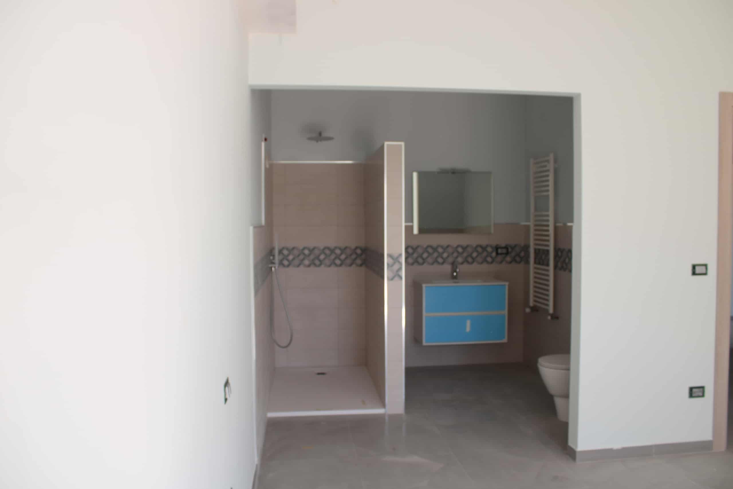 Lavanderia moderna con doccia e lavabo, pareti in ceramica beige, spazio funzionale e arredi di design, ideale per case in vendita e affitto, soluzioni abitative moderne NextCasa.