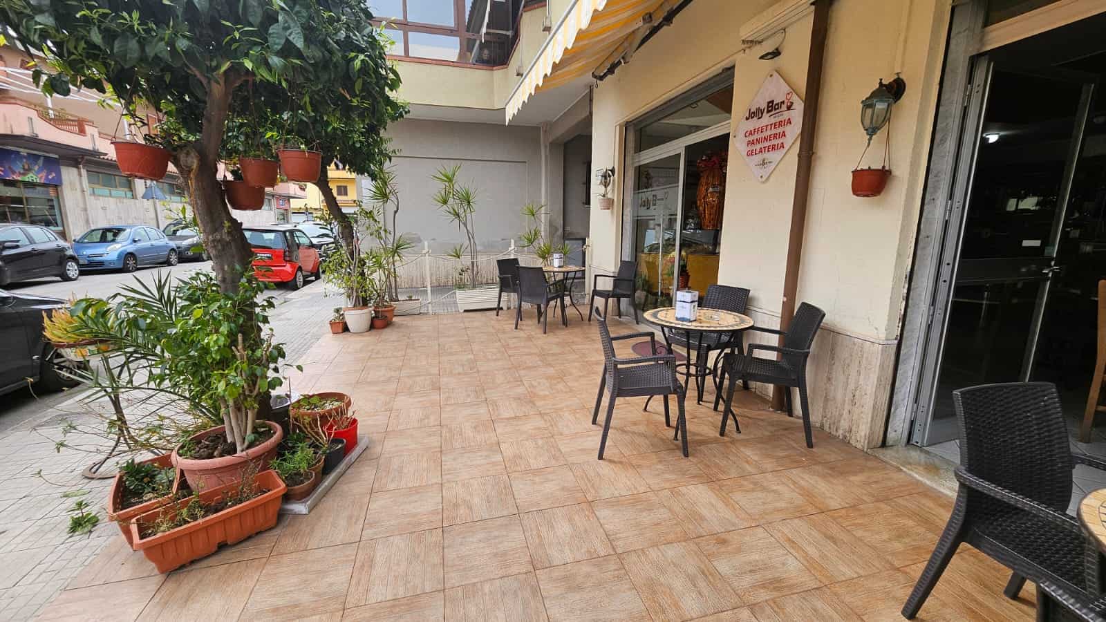 Spazio esterno di caffetteria con tavoli e sedie in un ambiente accogliente, decorato con piante e fiori, ideale per relax e convivialità, promuovendo servizi di caffetteria e ristorazione all'aperto.