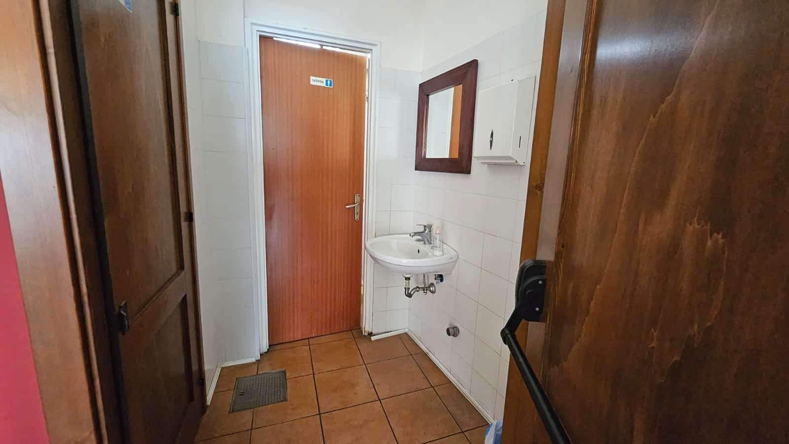 Lavandino e porta del bagno in un appartamento, finiture in legno e piastrelle bianche, ambiente funzionale e accogliente, ideale per affitti brevi o residenziali nel contesto di NextCasa.