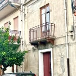 Balcone in ferro battuto su stabile storico in centro città, con vista su veicolo in primo piano, pareti in pietra e strada urbana, stile architettonico tradizionale italiano.