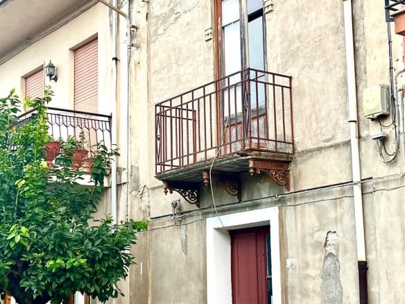 Balcone in ferro battuto su stabile storico in centro città, con vista su veicolo in primo piano, pareti in pietra e strada urbana, stile architettonico tradizionale italiano.